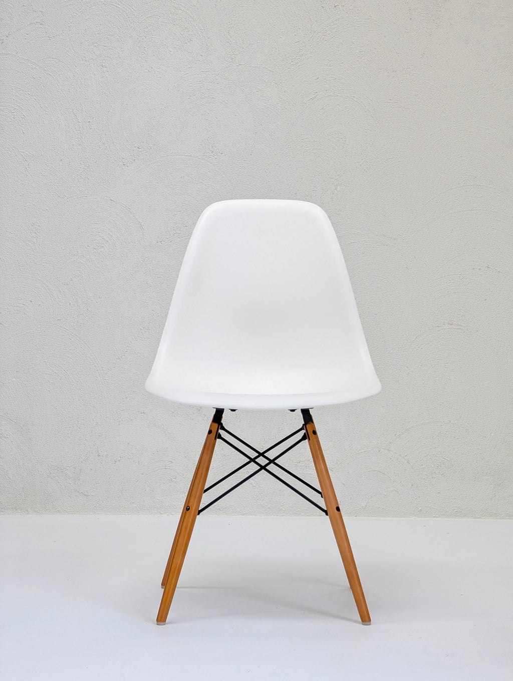 Modern white plastic chair with wooden legs and black metal supports against textured white wall