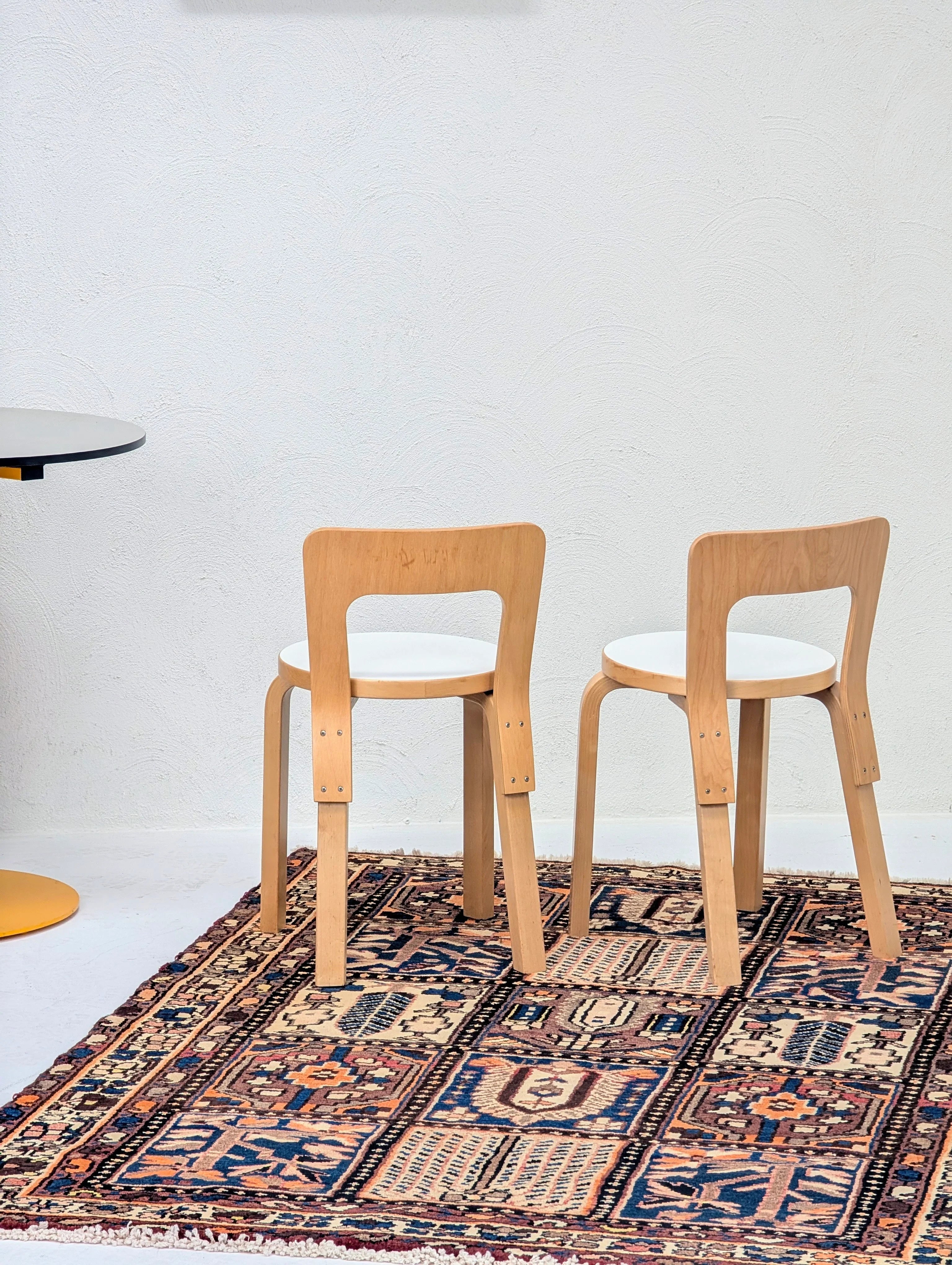 Two wooden chairs with white seats on a patterned rug against a white textured wall