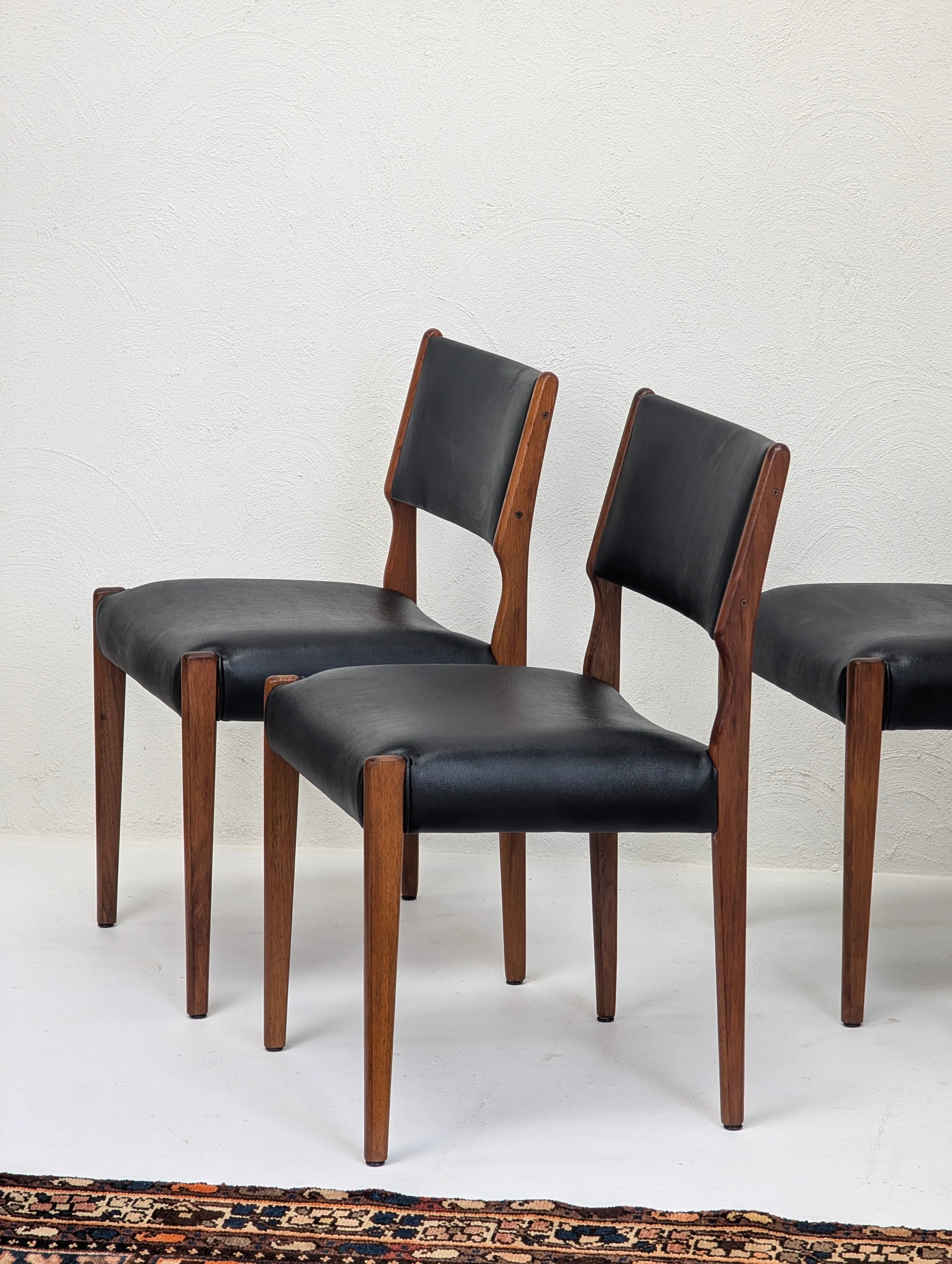 Set of mid-century modern dining chairs with black leather seats and wooden frames on white floor