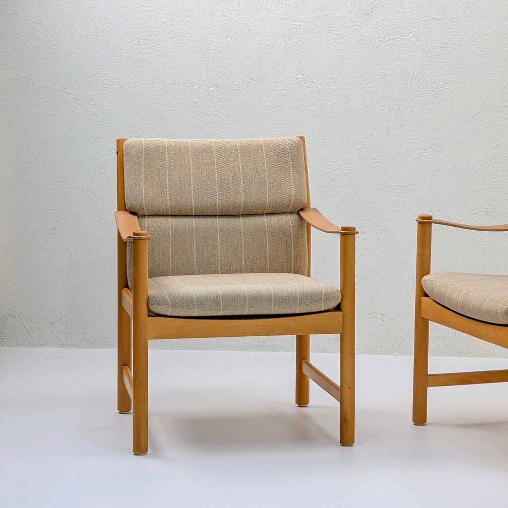 Mid-century modern wooden armchair with beige upholstered seat and backrest against a textured white wall.