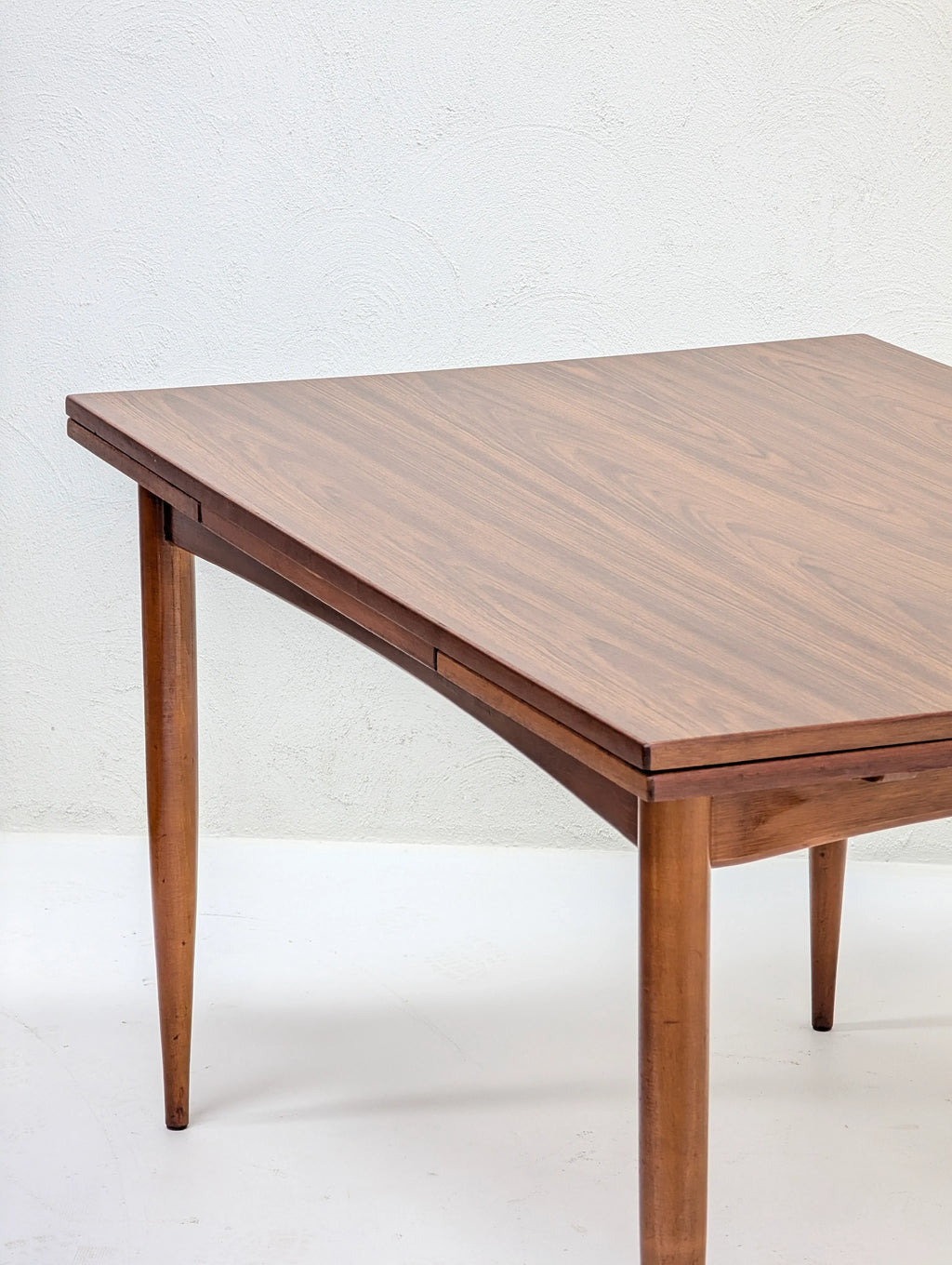 Mid-century modern wooden dining table with tapered legs against white wall