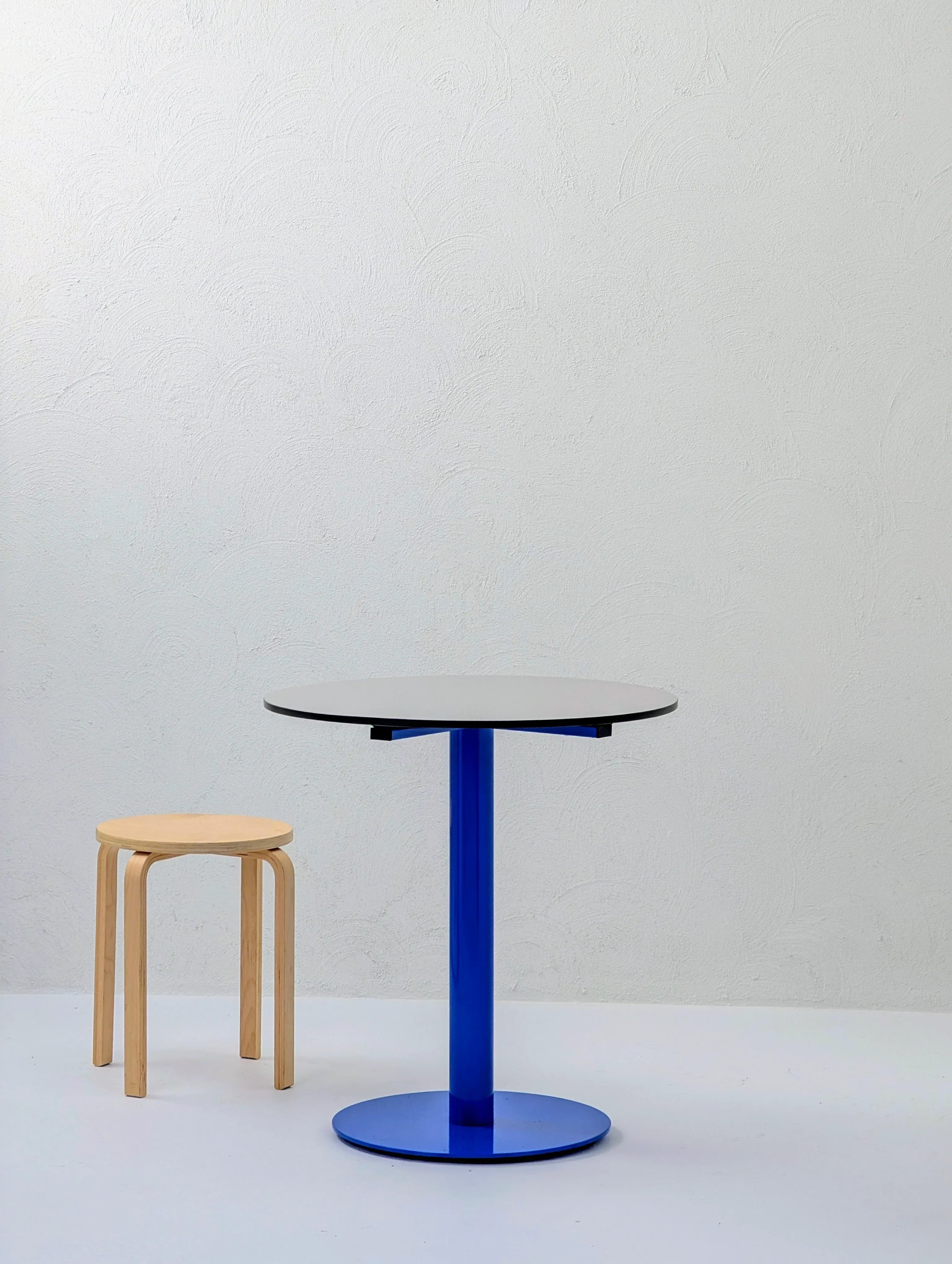 Minimalist scene with a light wooden stool and a round blue pedestal table on a white background