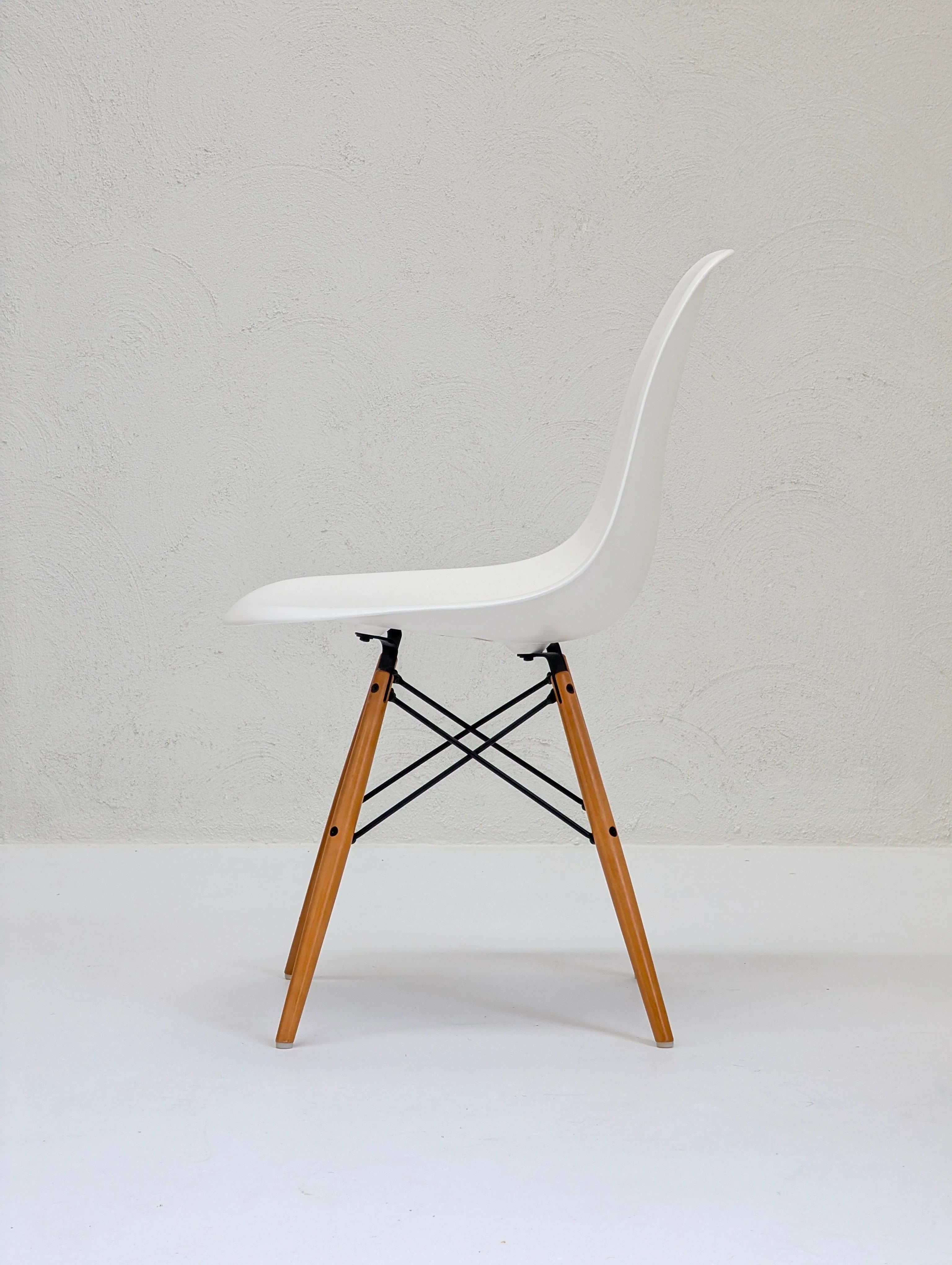Modern white plastic chair with wooden legs and black metal supports on white floor