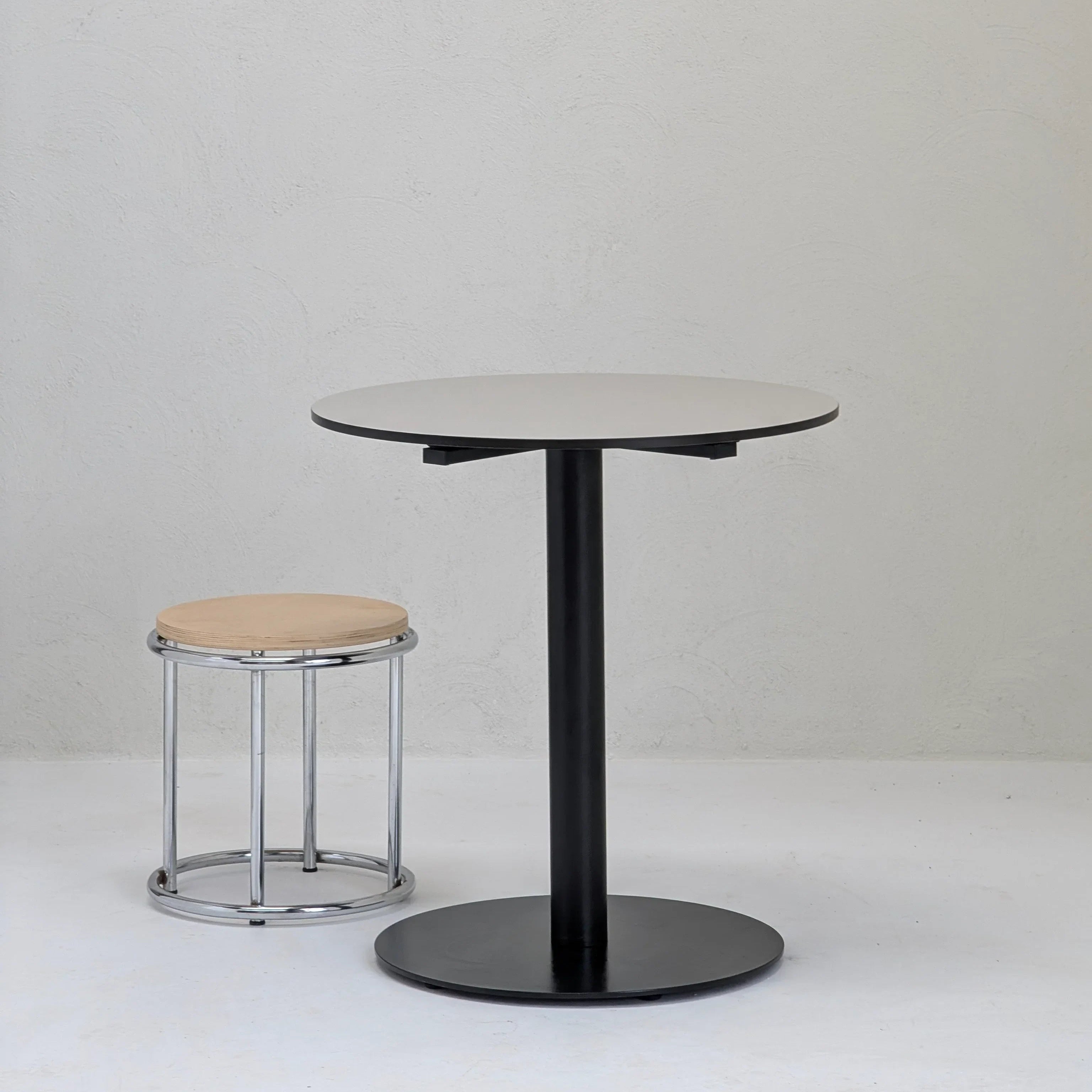 Minimalist round black table with metal stool and wooden seat in modern white room