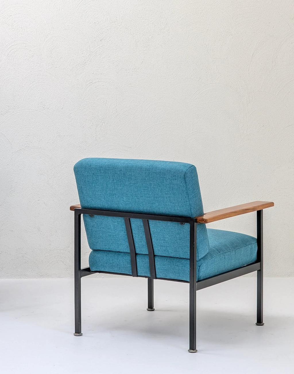 Modern blue upholstered armchair with metal frame and wooden armrests against white wall