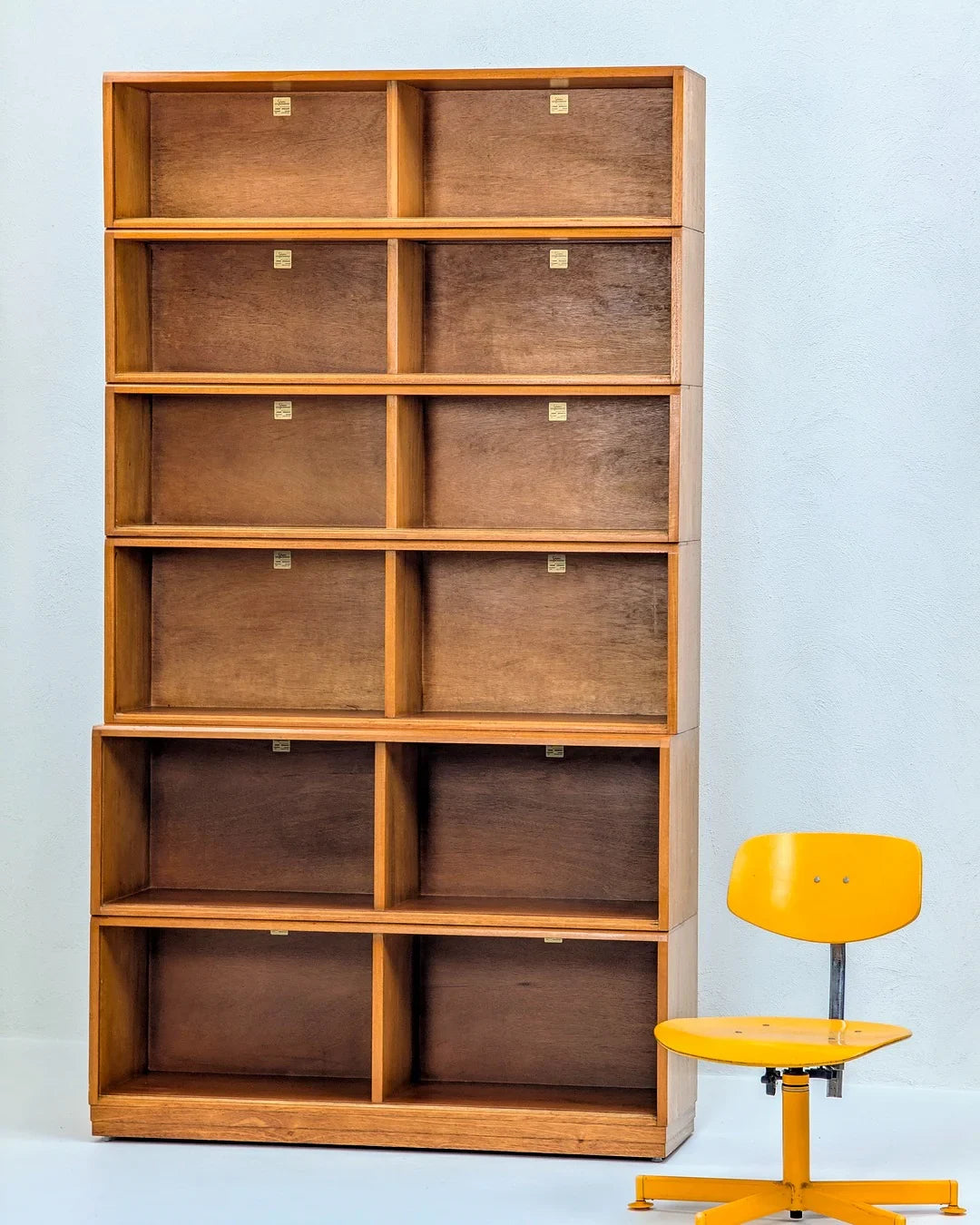 Vintage wooden bookshelf with cubby compartments beside a yellow swivel chair on white wall