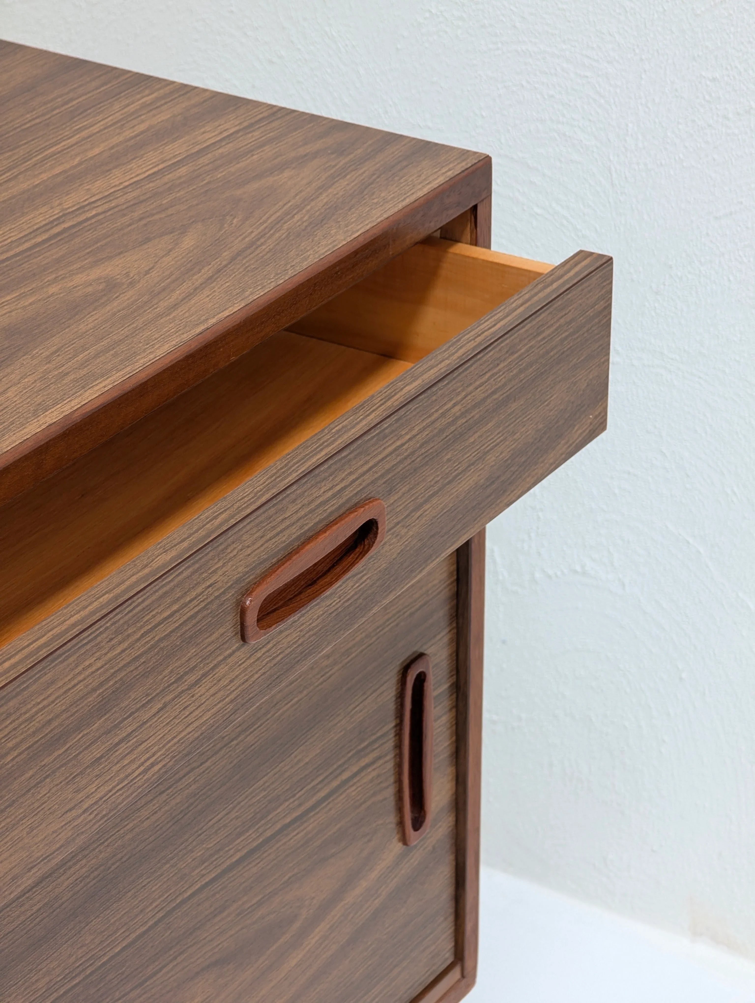 Close-up of an open drawer in a modern wooden cabinet with a smooth wood grain finish