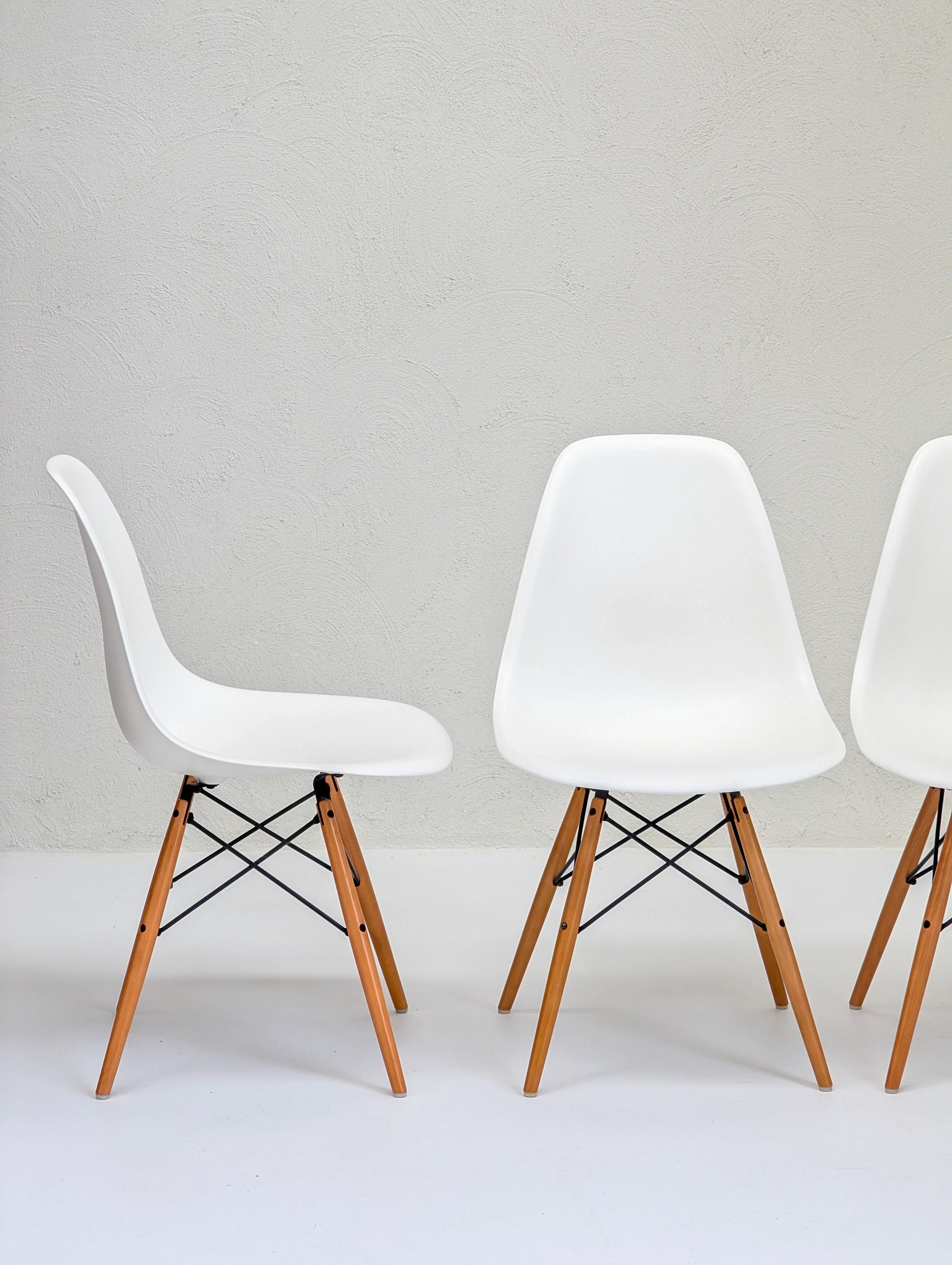 Modern white chairs with wooden legs against a textured light gray wall