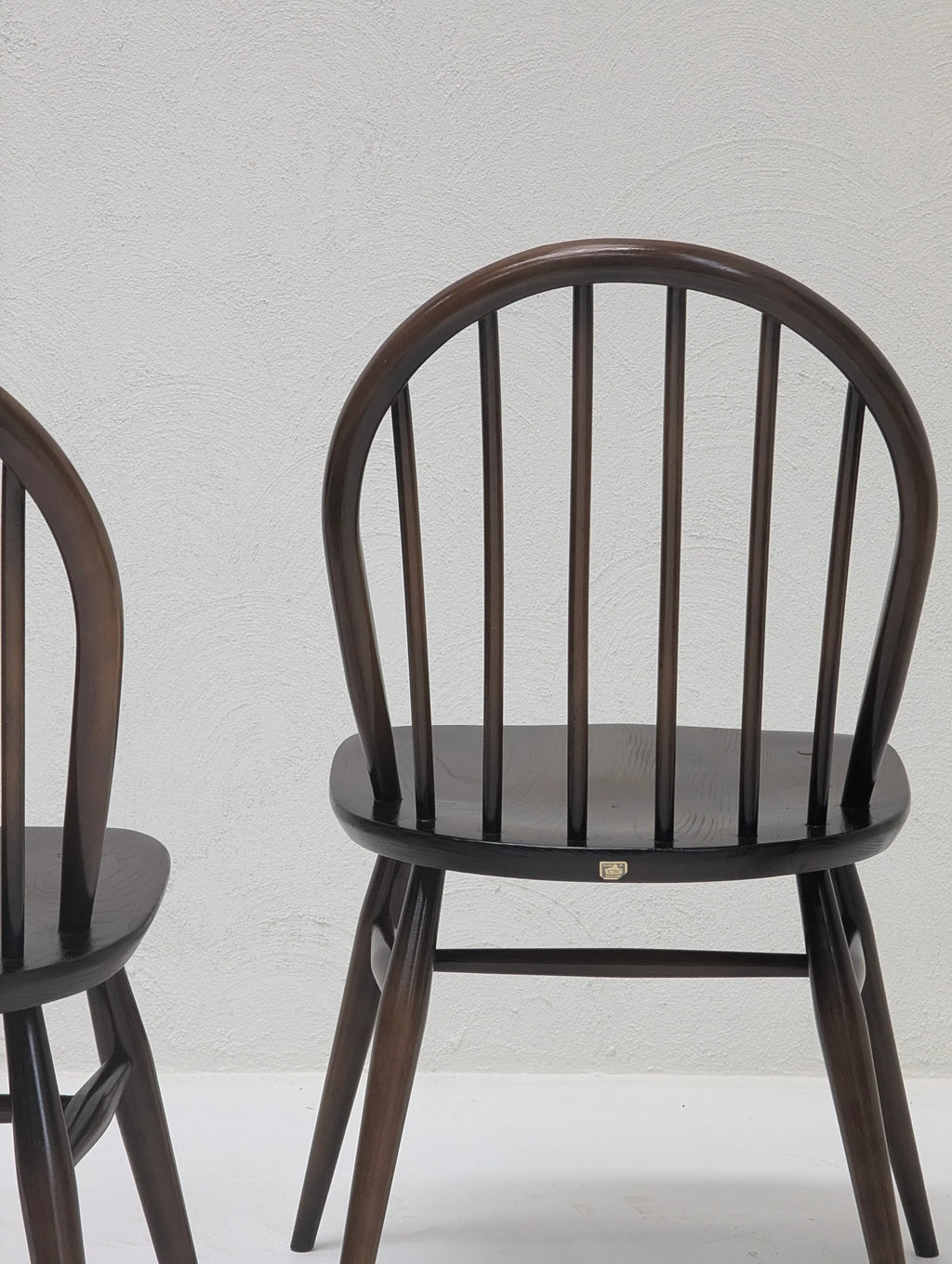 Dark wooden spindle-back dining chair with curved arch backrest against textured white wall