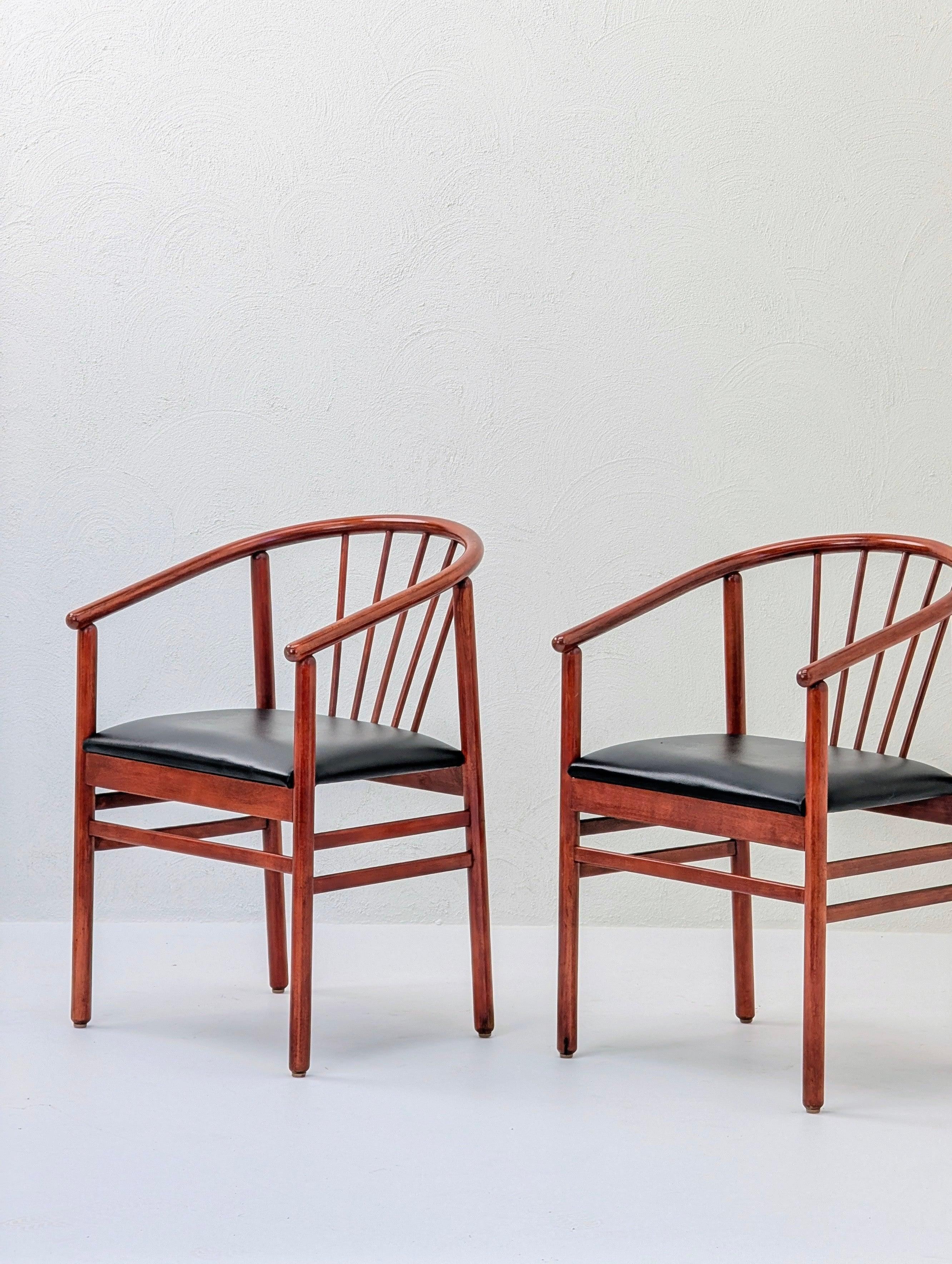 Pair of modern wooden armchairs with black cushioned seats against a white wall