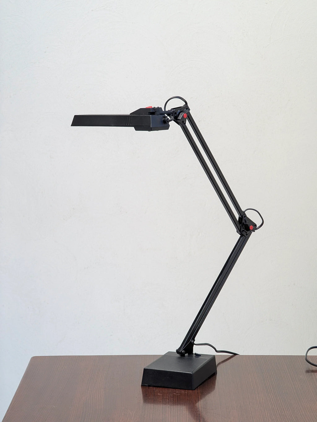 Modern black adjustable desk lamp on wooden table against plain white wall