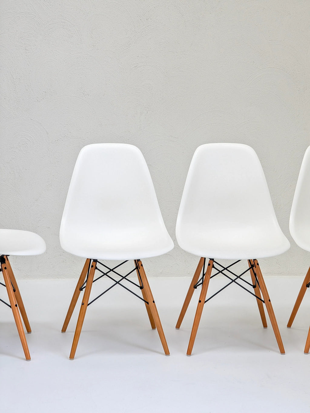 Modern white plastic chairs with wooden legs against a textured light grey wall