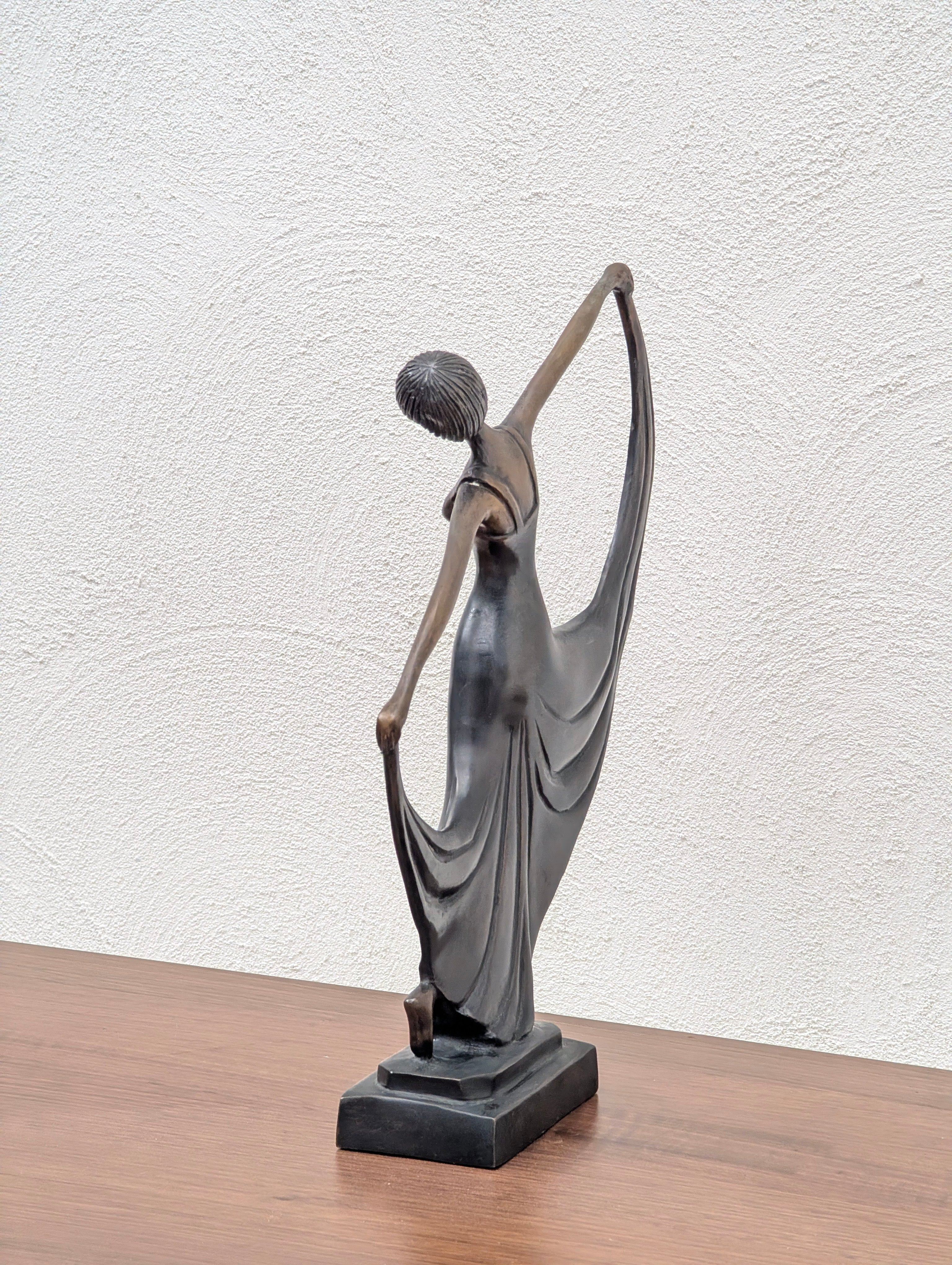 Bronze statue of a woman in flowing dress posed with arms raised, standing on wooden surface