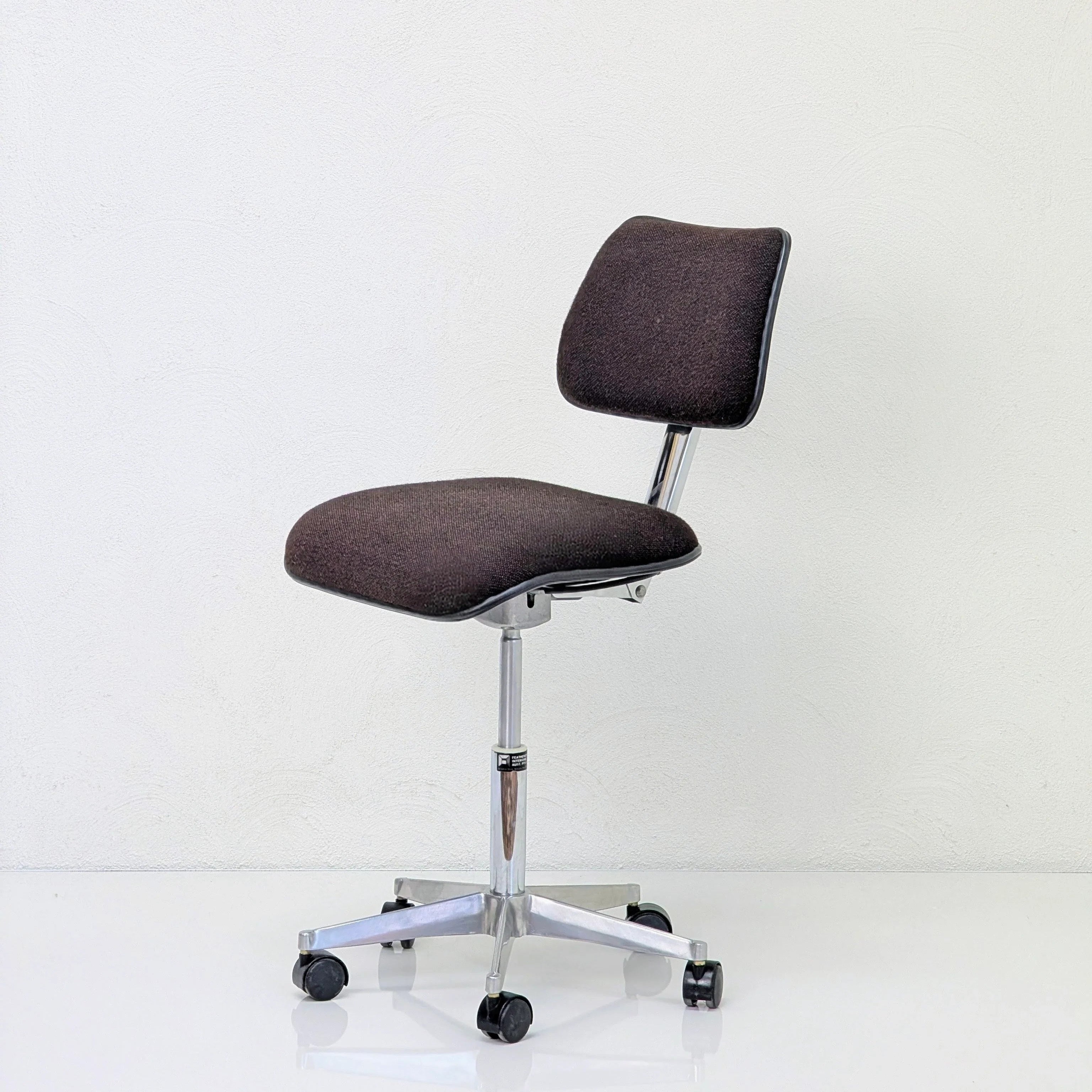 Black office chair with cushioned backrest and seat on chrome wheeled base against white wall