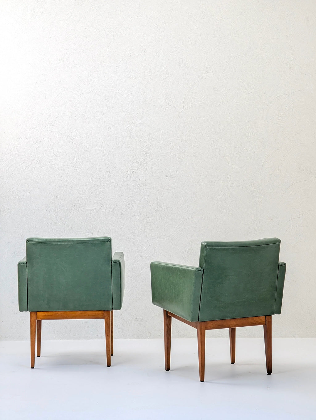 Two green mid-century modern armchairs with wooden legs in a minimalist setting