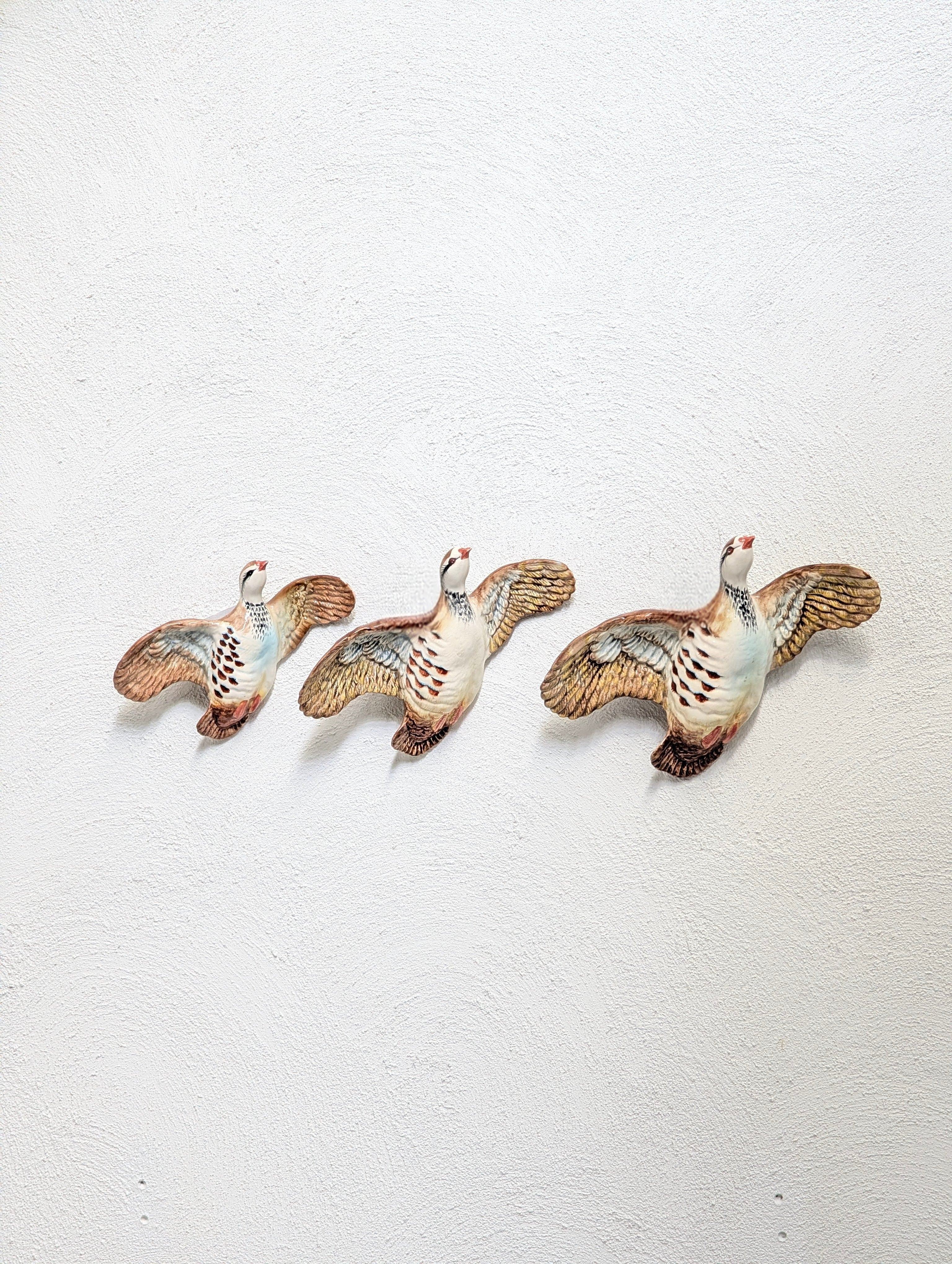 Three decorative ceramic birds with outstretched wings mounted on a textured white wall