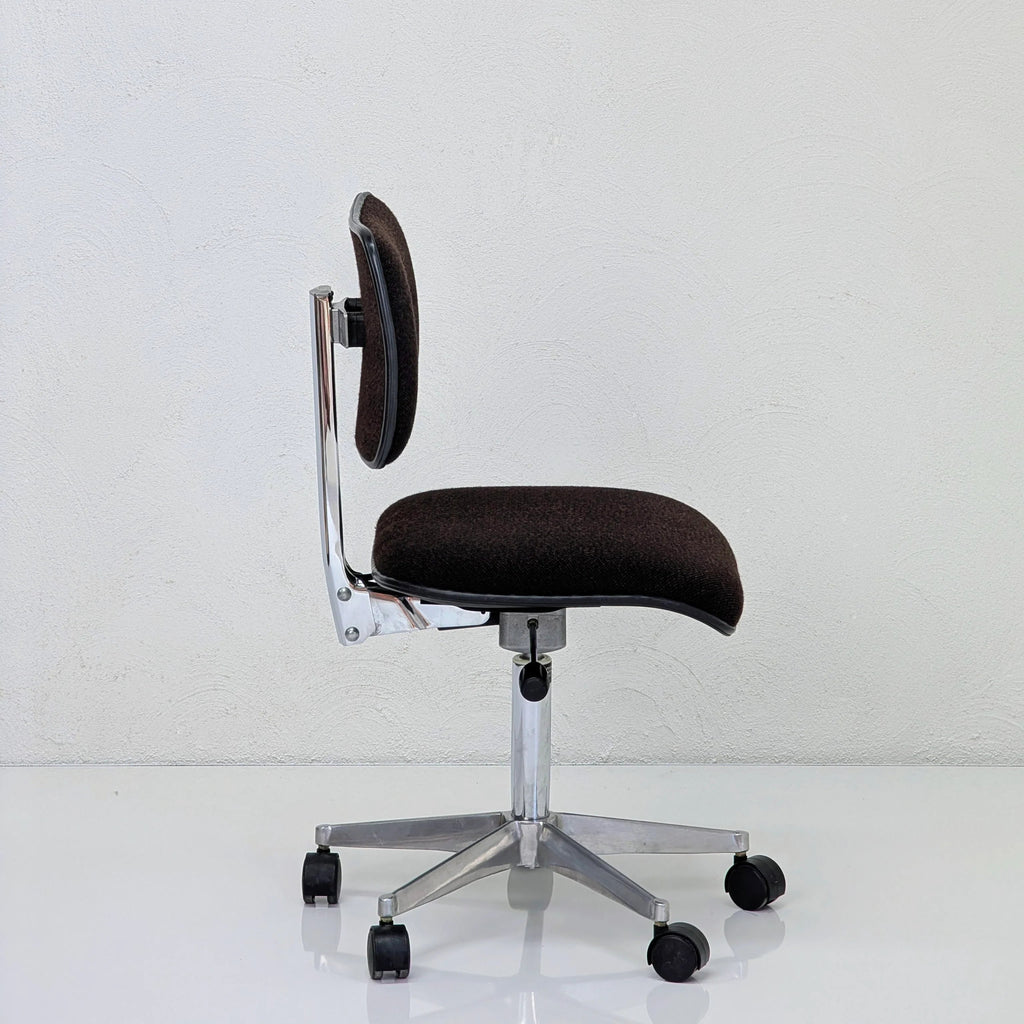 Side view of a modern black office chair with chrome base and wheels on a glossy white floor