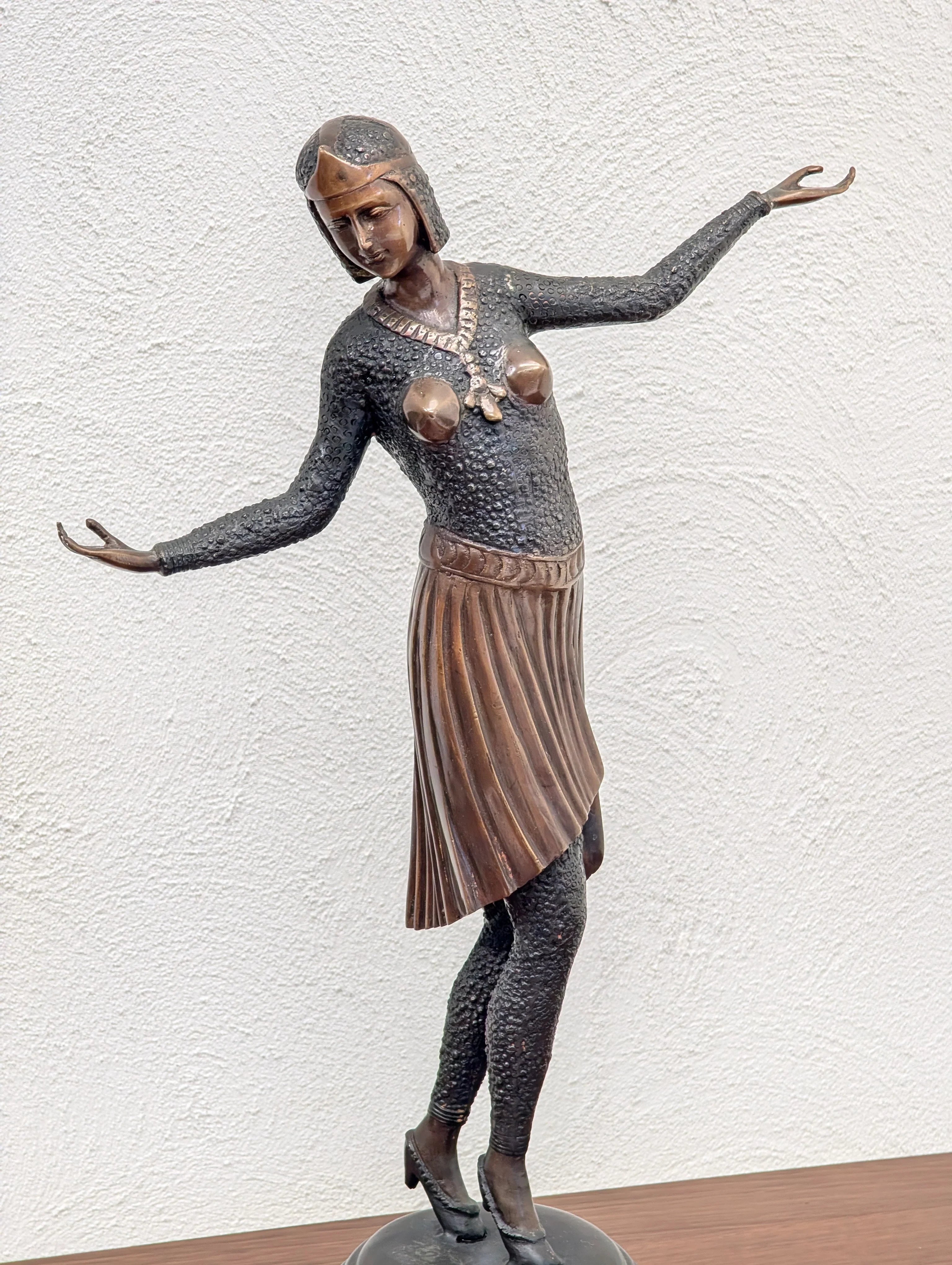 Bronze Art Deco sculpture of a woman in pleated skirt and patterned top with outstretched arms on wooden surface