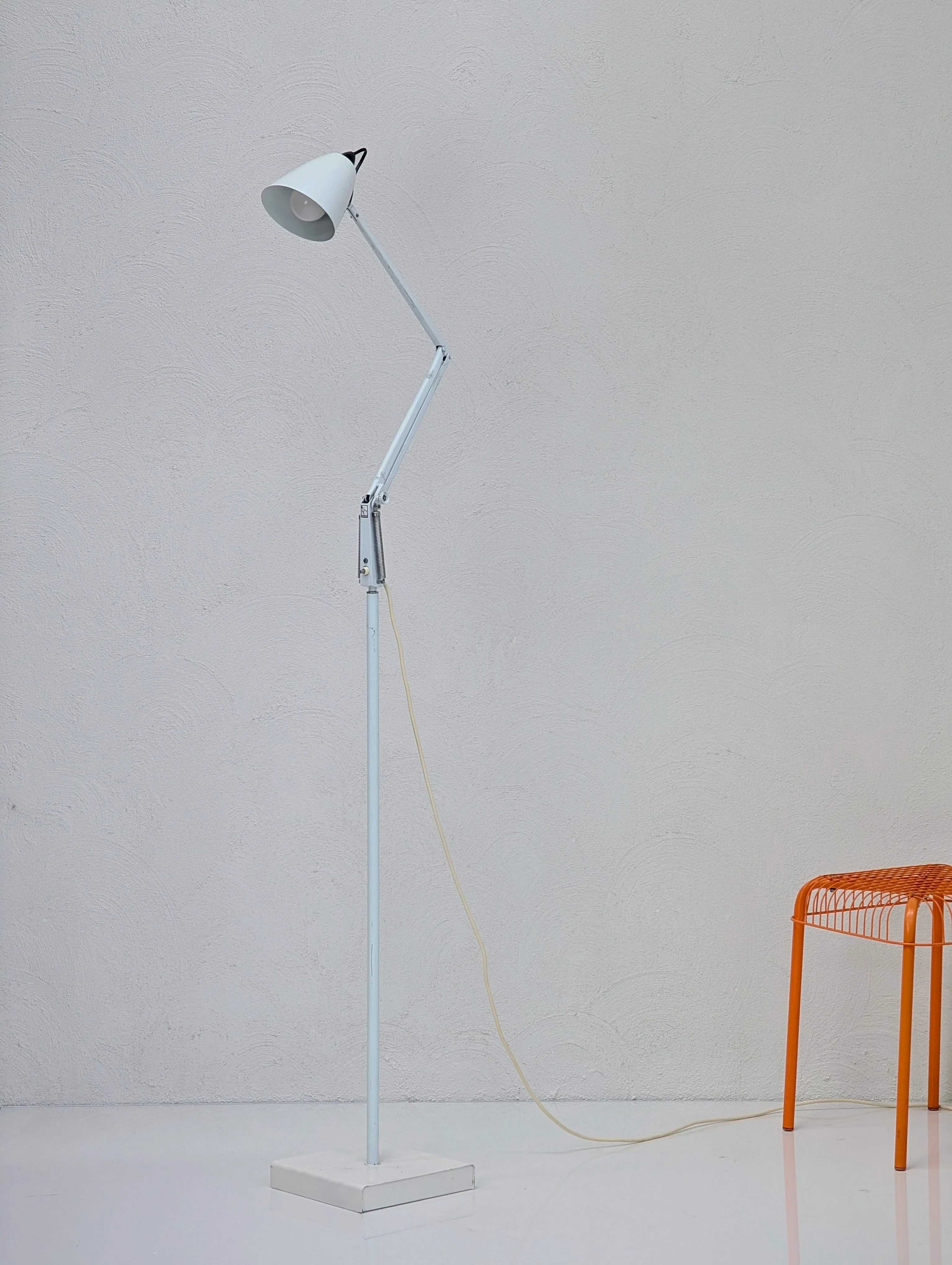 Minimalist white adjustable floor lamp with exposed cord next to an orange metal wire stool on glossy floor