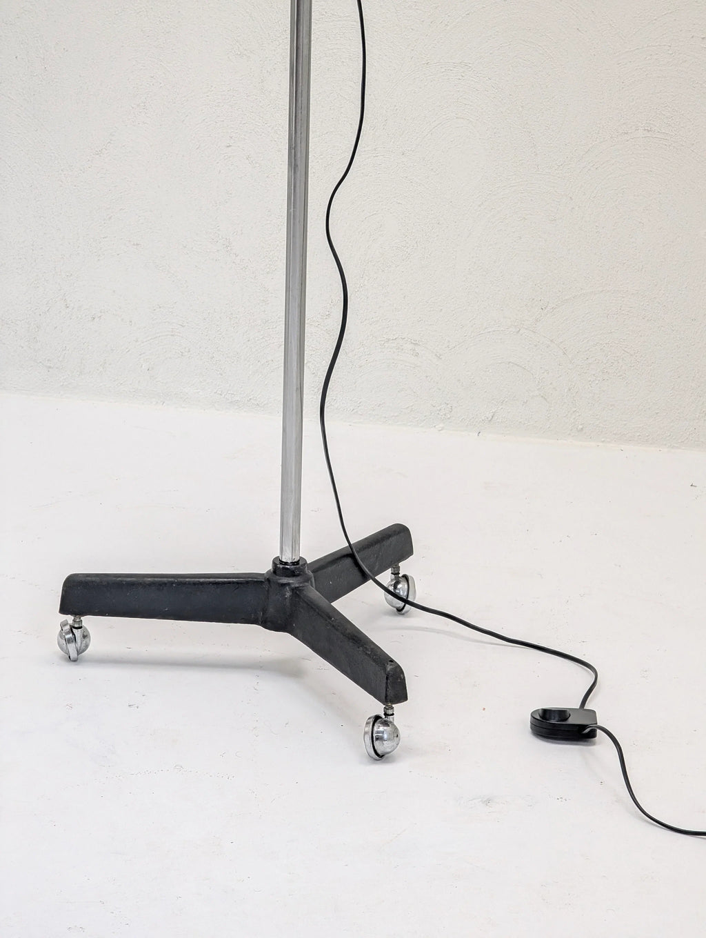 Metal stand with caster wheels and a black power cord on a white floor, minimalist style