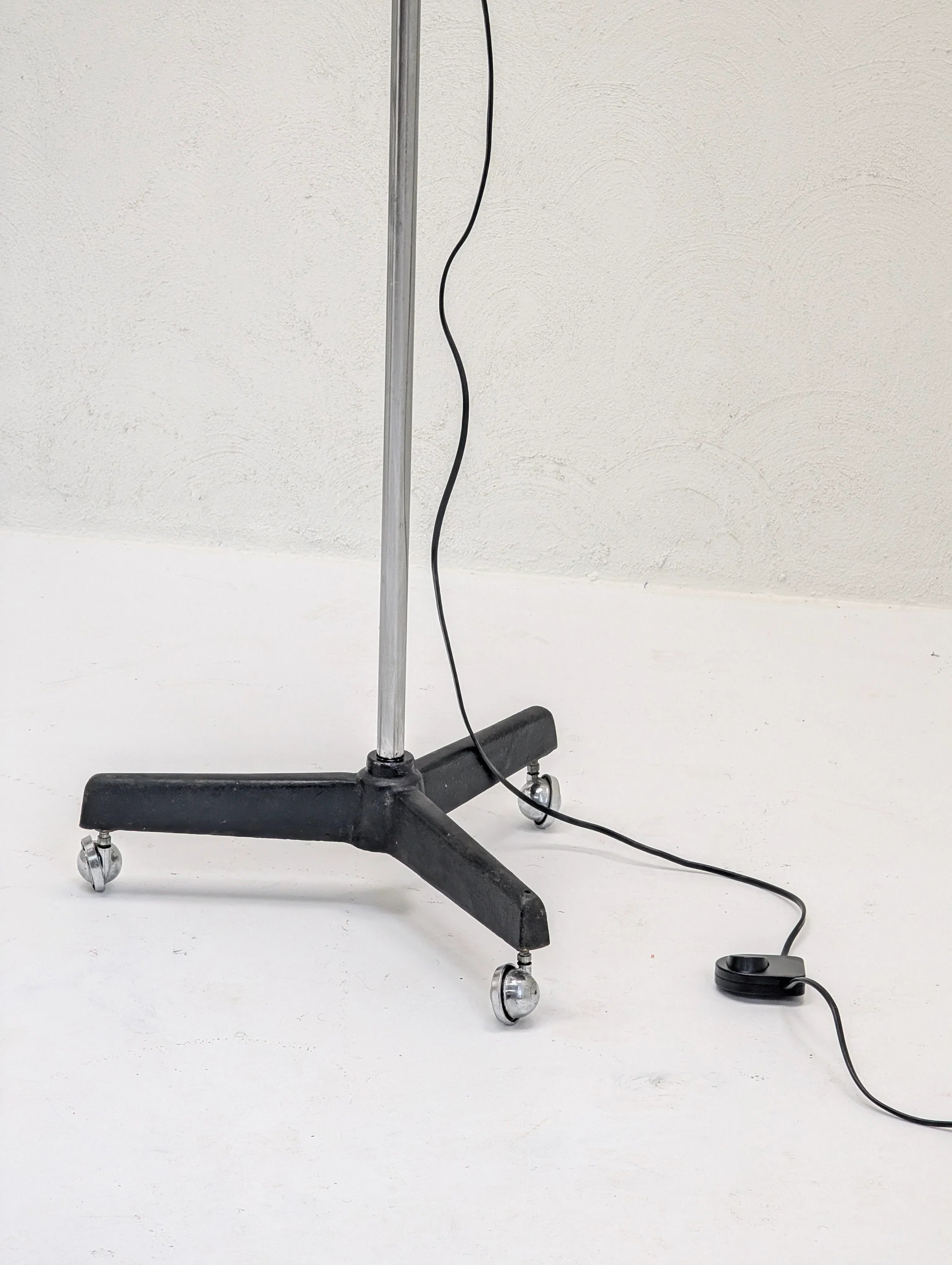 Metal stand with caster wheels and a black power cord on a white floor, minimalist style