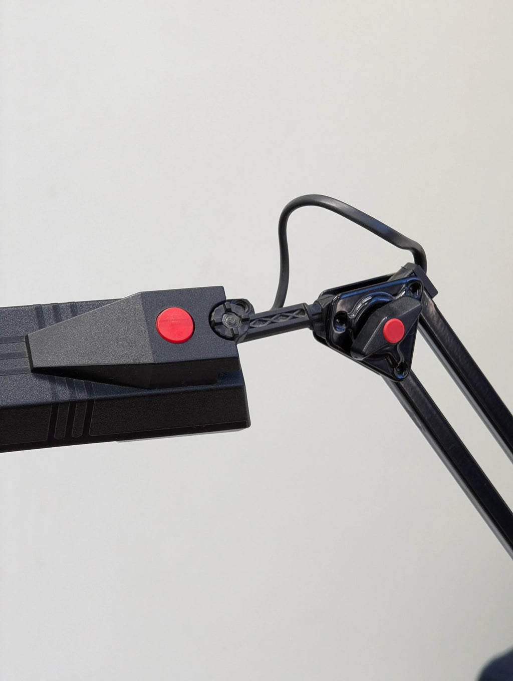 Close-up of adjustable black desk lamp arm with red accent buttons against a plain background