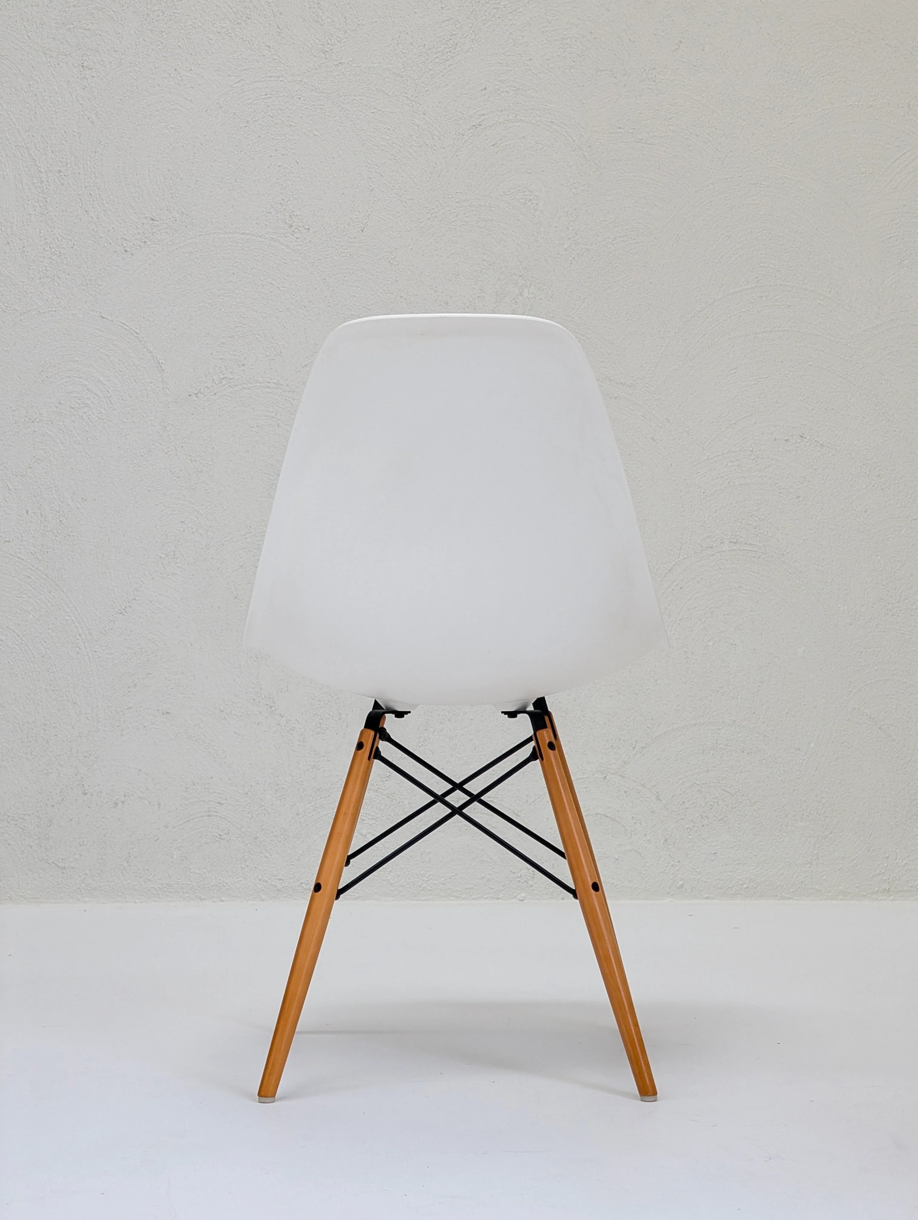 Minimalist white modern chair with wooden legs and black metal supports against textured wall