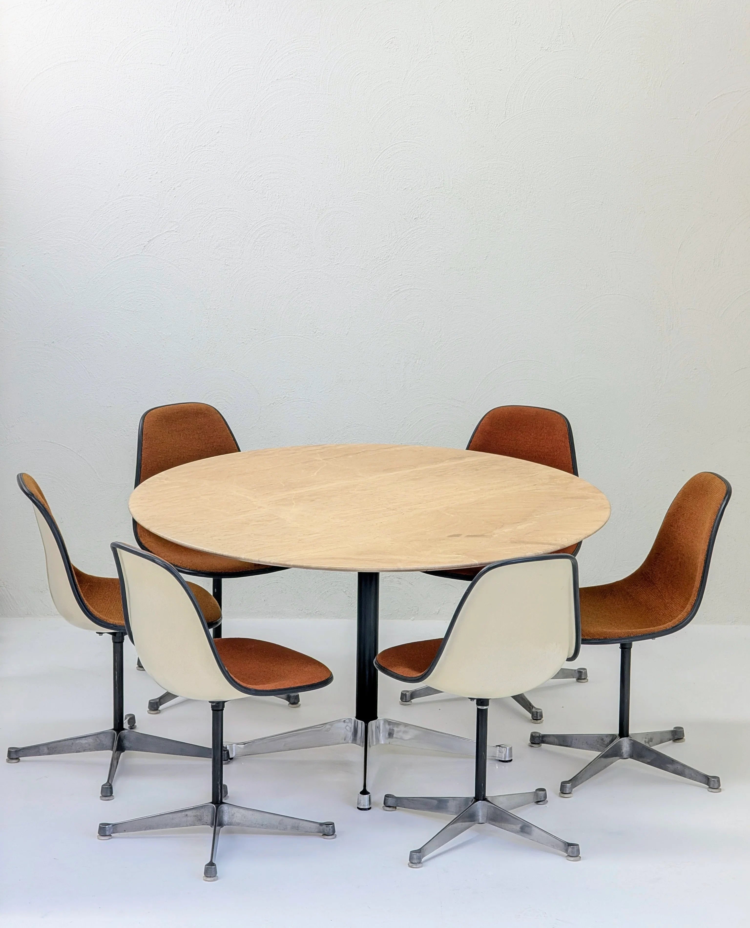 Round light wood table surrounded by six retro swivel chairs with brown cushions and white backs