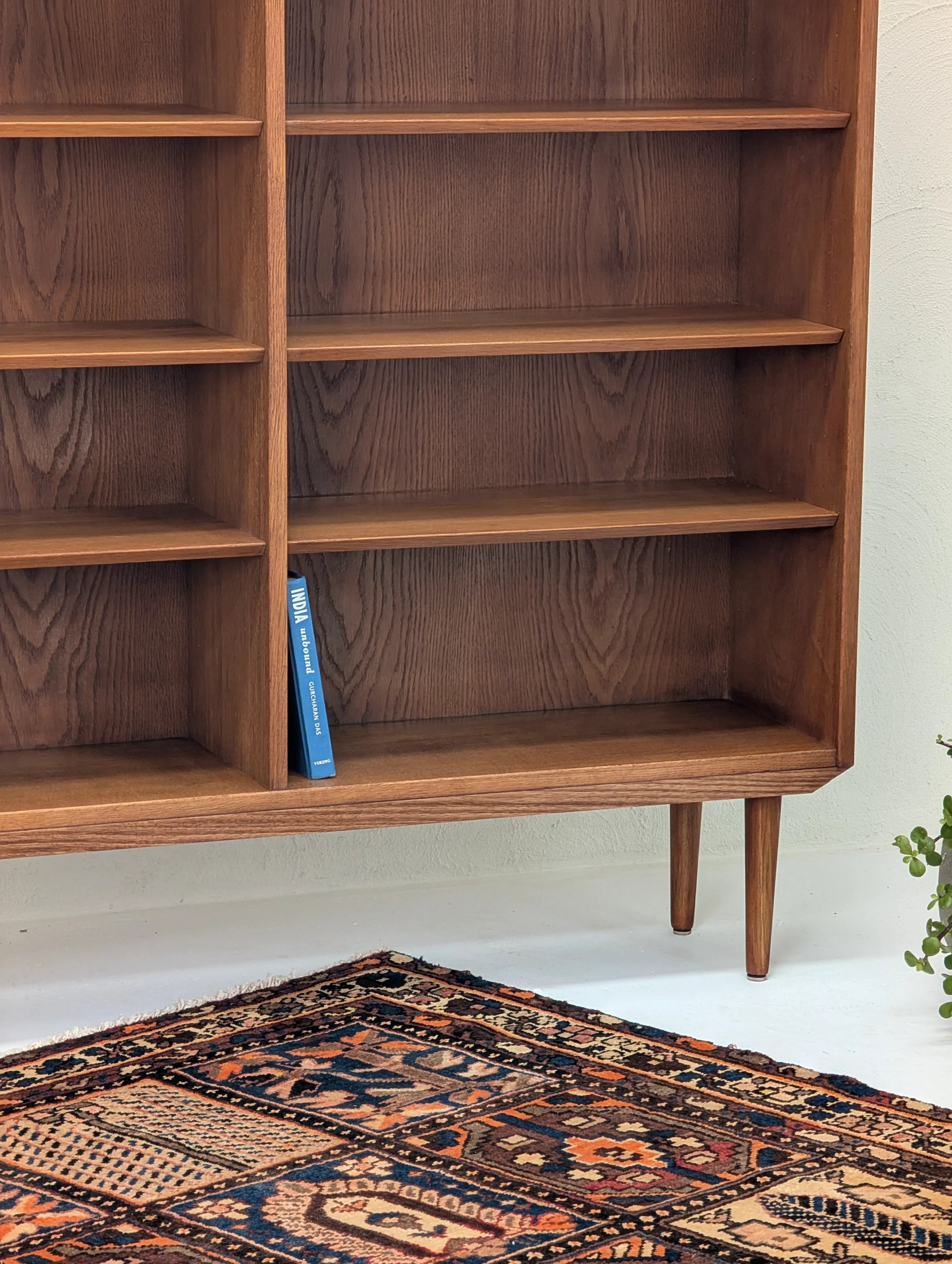 Mid-century modern wooden bookshelf with a single blue book and a patterned rug on white floor