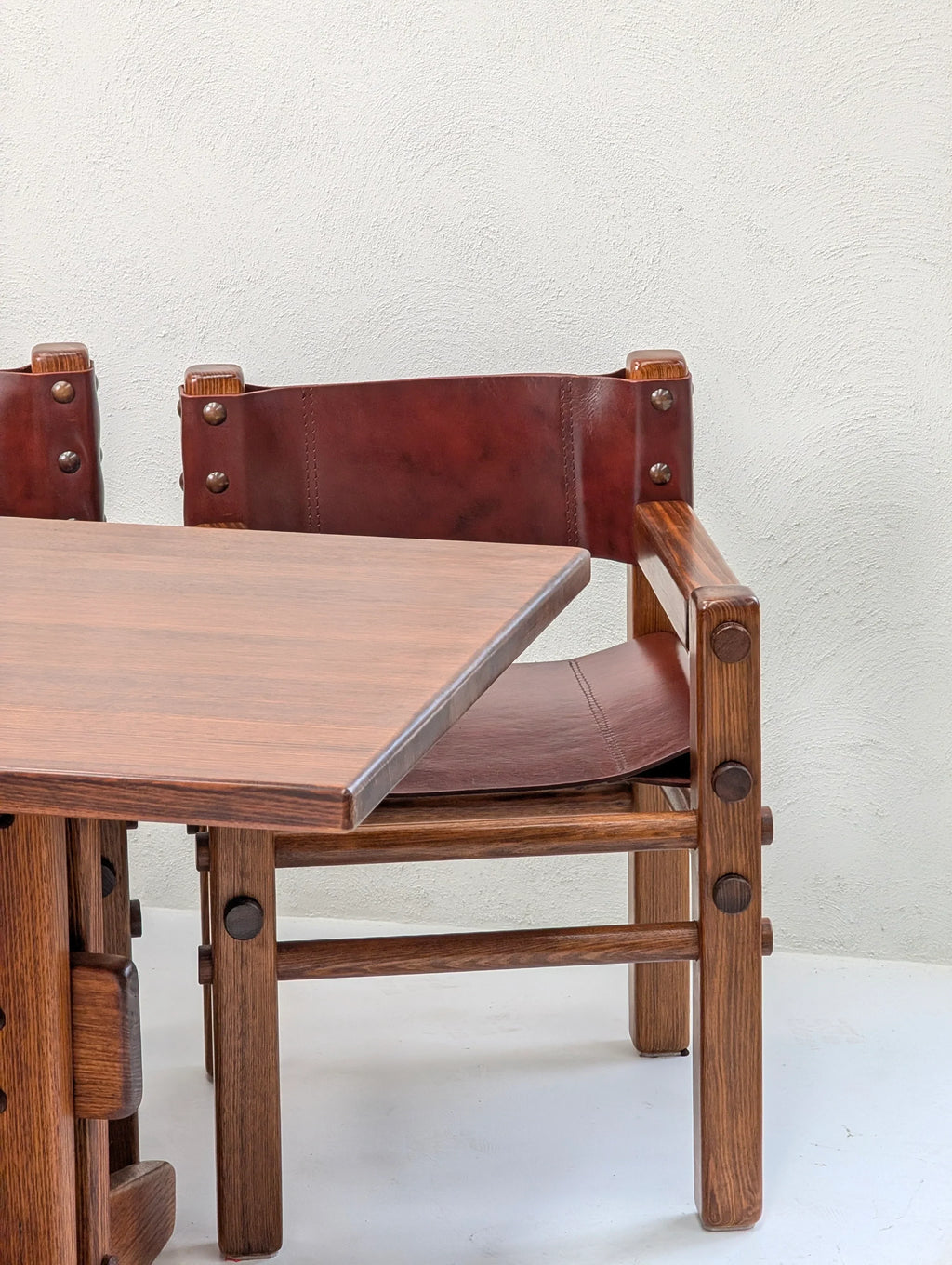 Wooden dining chair with brown leather backrest beside matching wood table on white background