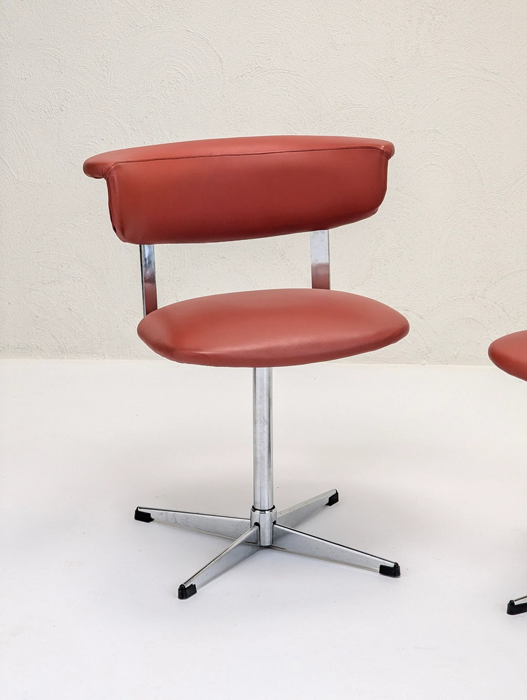 Modern red leather office chair with curved backrest and metal base on white floor