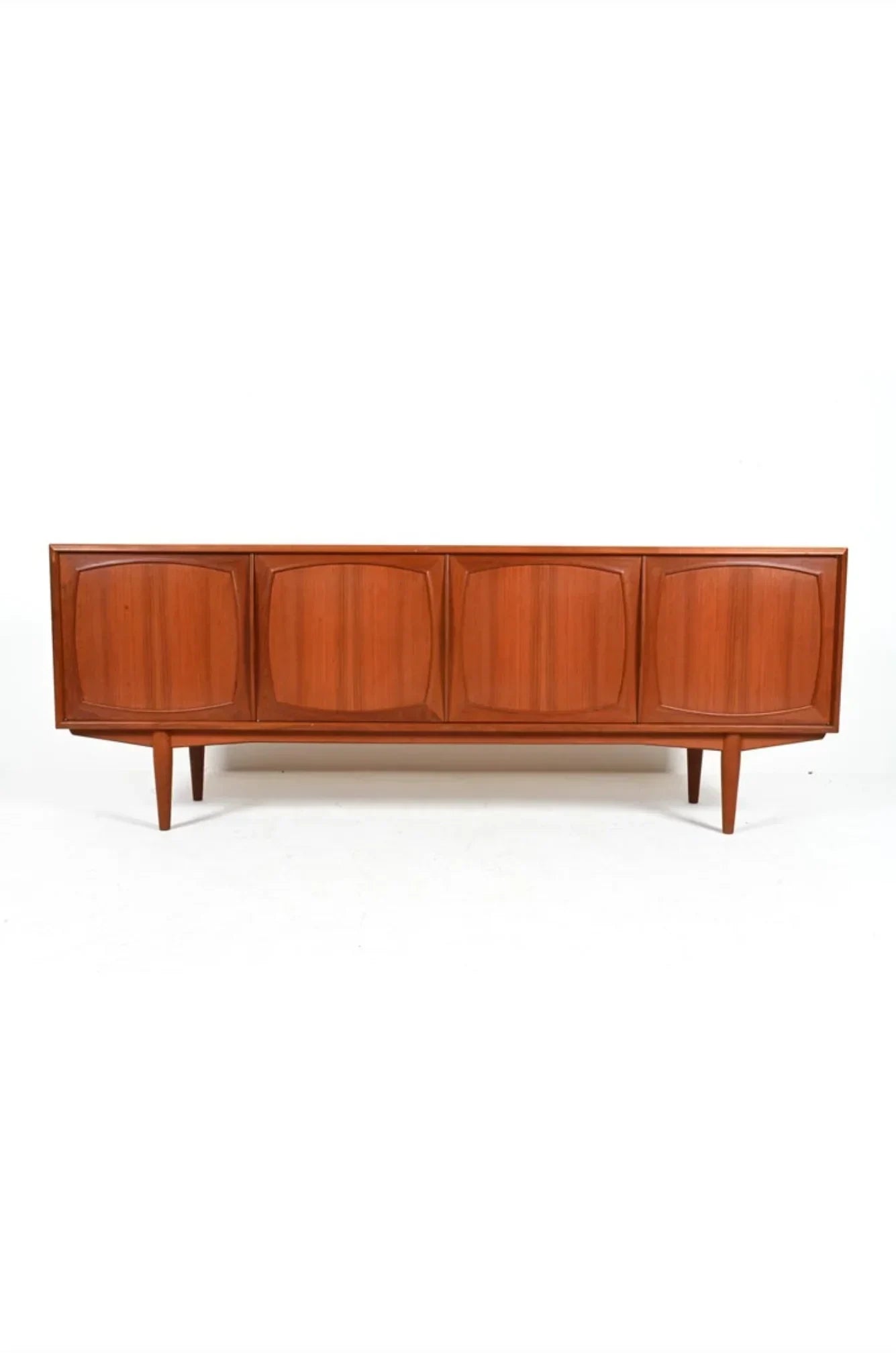 Mid-century modern teak sideboard with four paneled doors and tapered legs on white background
