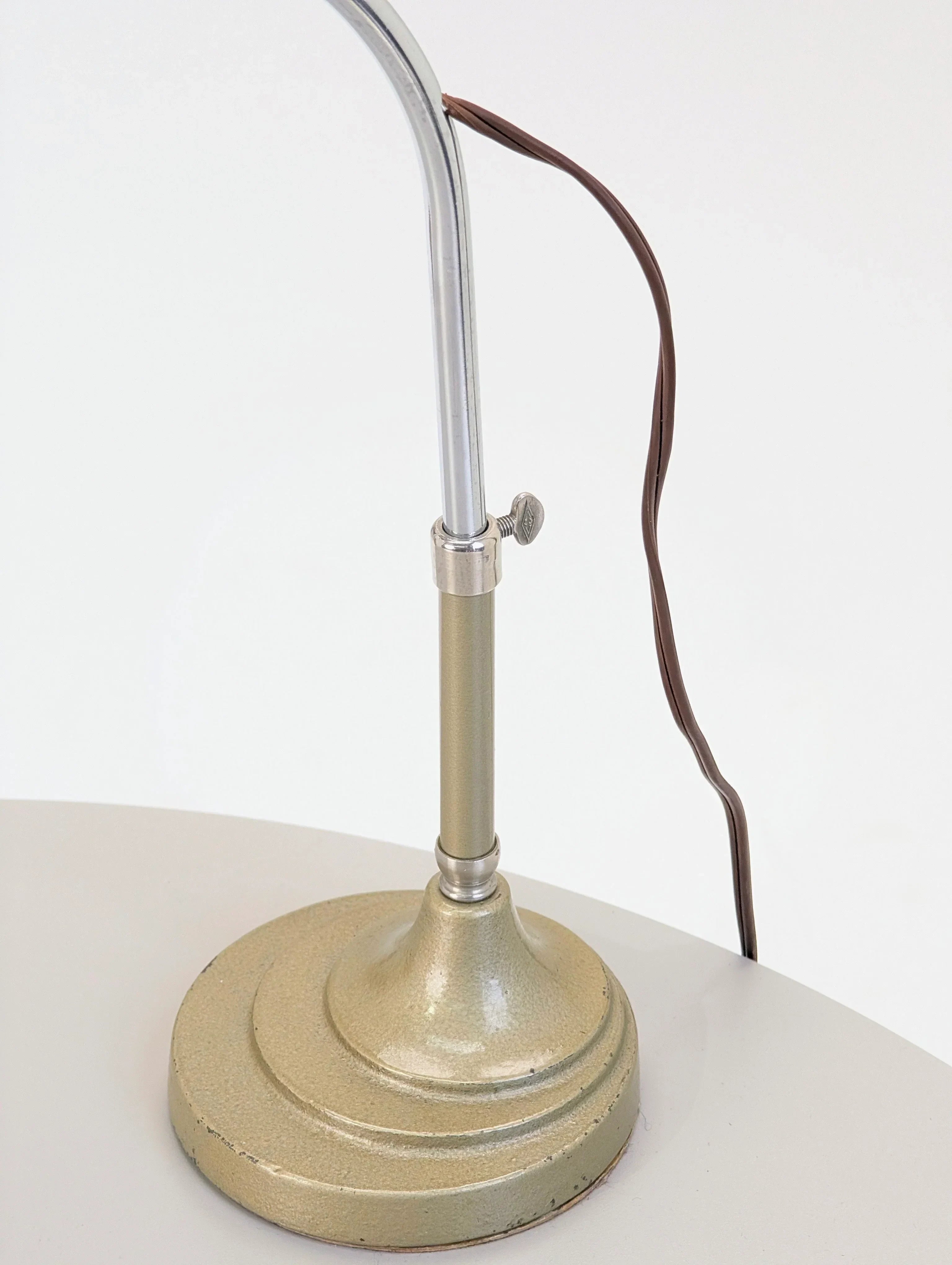 Vintage metal desk lamp base with curved chrome stem and brown cord on white table