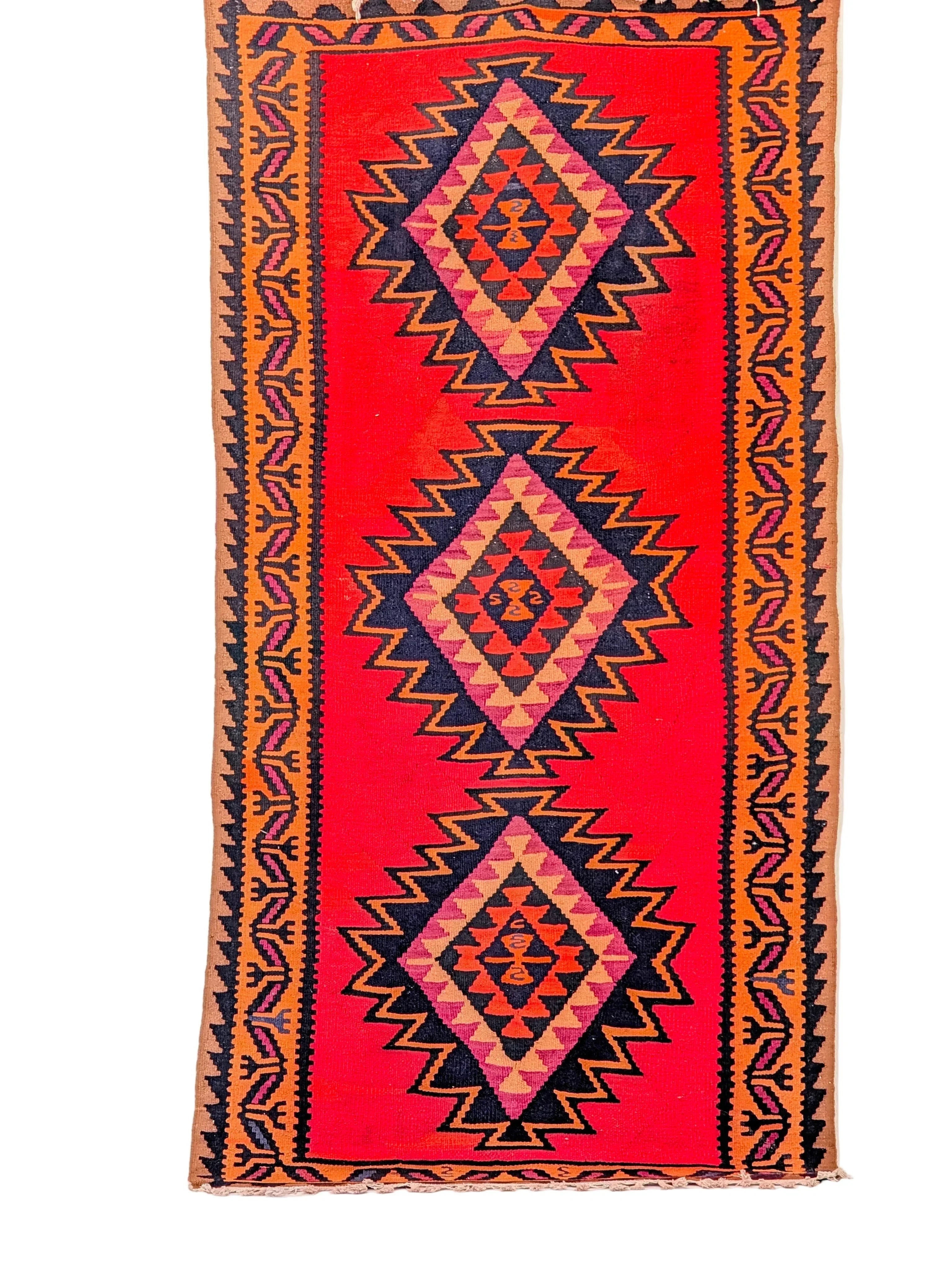 Handwoven kilim rug with geometric diamond patterns on a red background and decorative borders