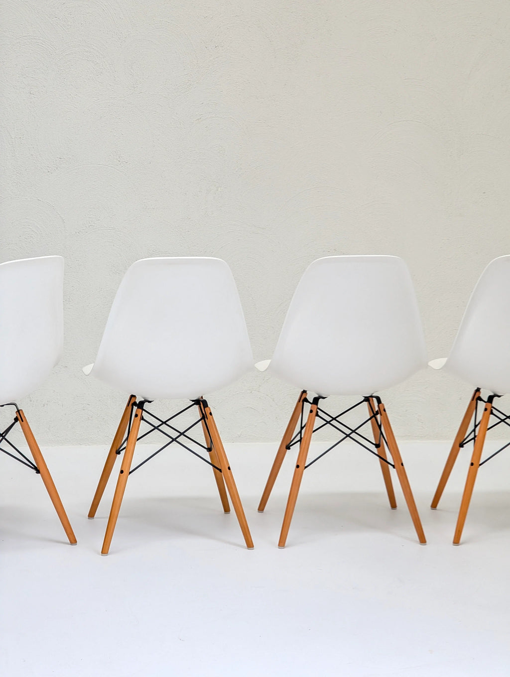 Four modern white plastic chairs with wooden legs in a minimal interior setting