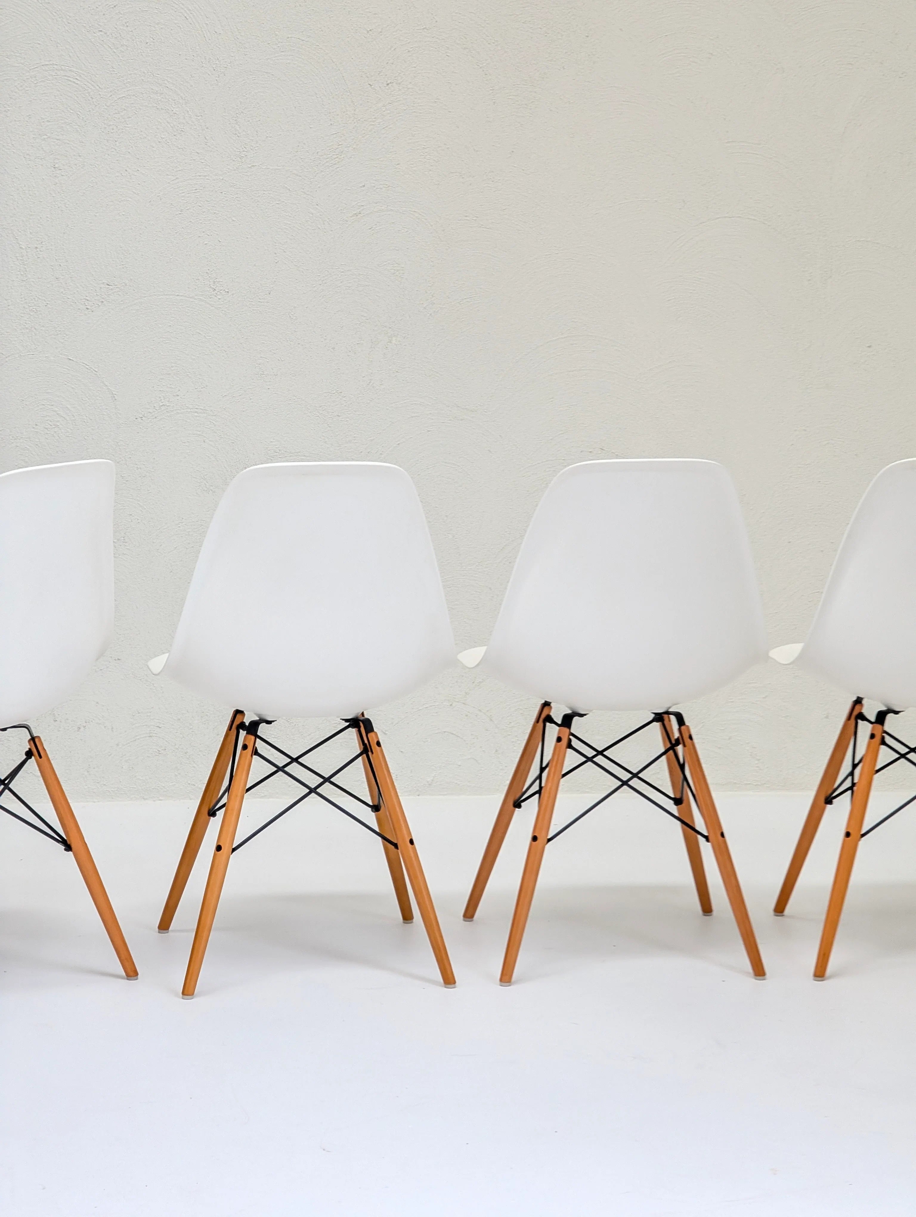 Four modern white plastic chairs with wooden legs in a minimal interior setting
