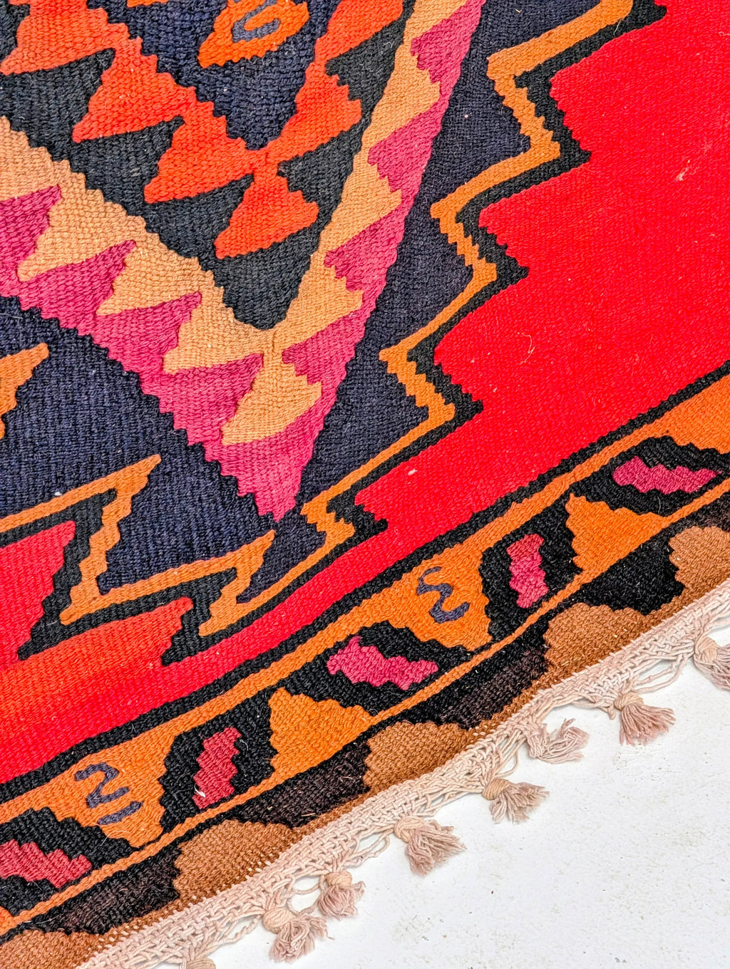 Colorful geometric kilim rug with red, pink, orange and black patterns and fringed edge
