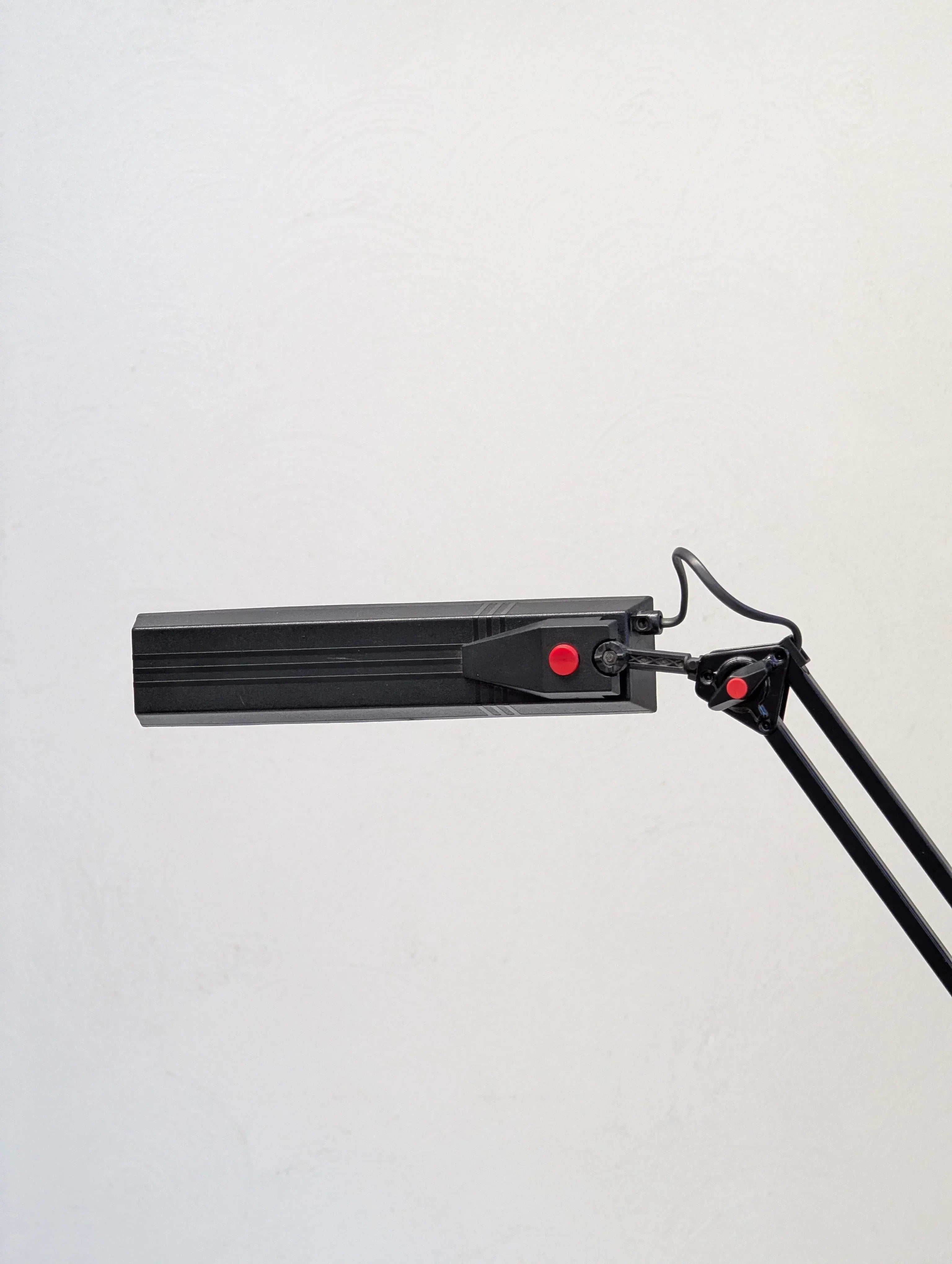 Black adjustable LED desk lamp with red accents against a white wall
