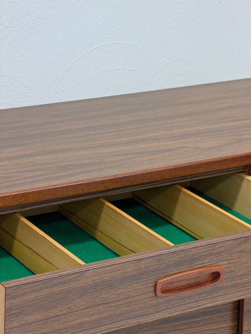 Wooden drawer with divided compartments lined in green felt inside a brown wooden cabinet