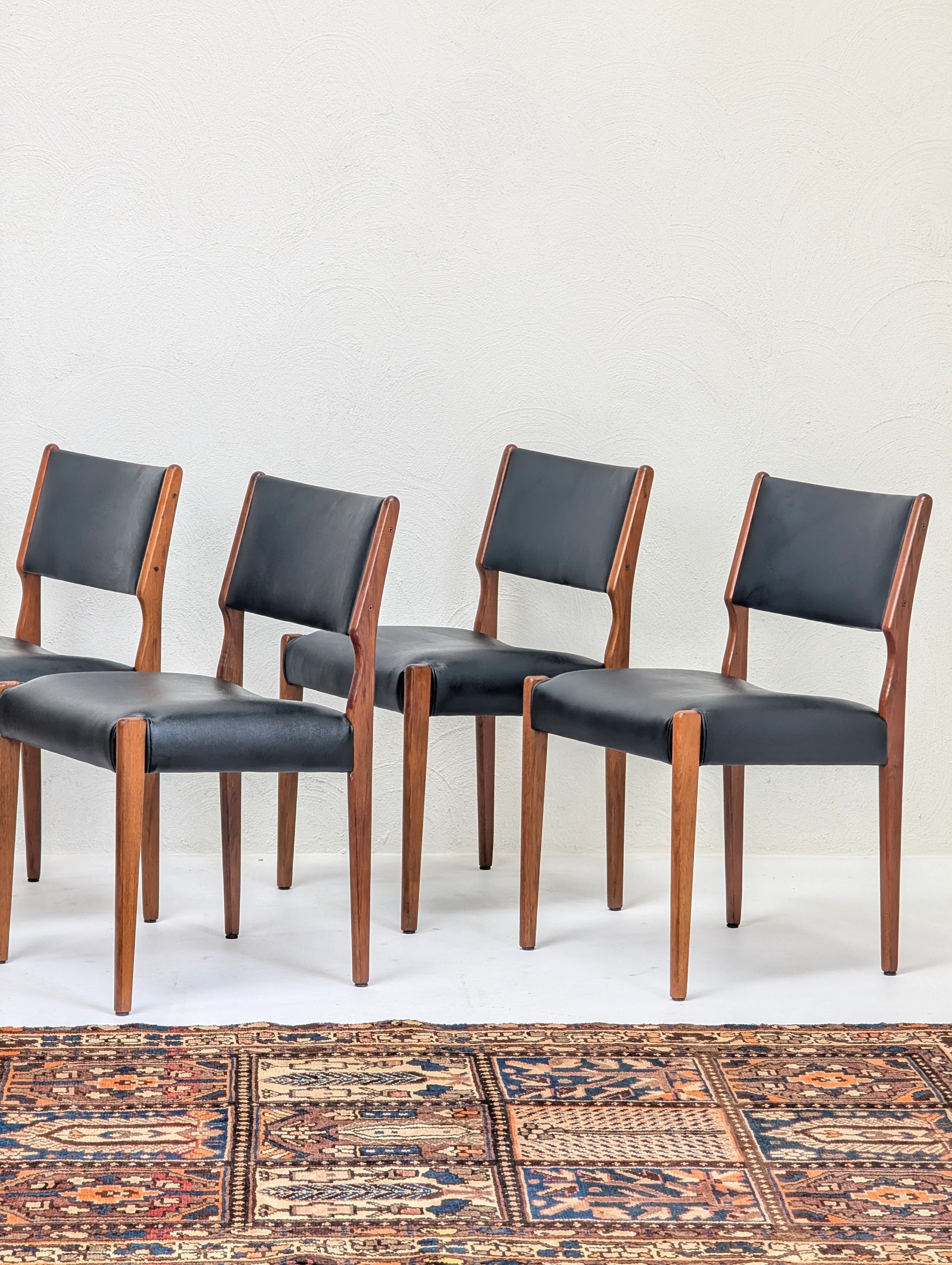 Set of four mid-century modern dining chairs with wooden frames and black leather cushions on a patterned rug