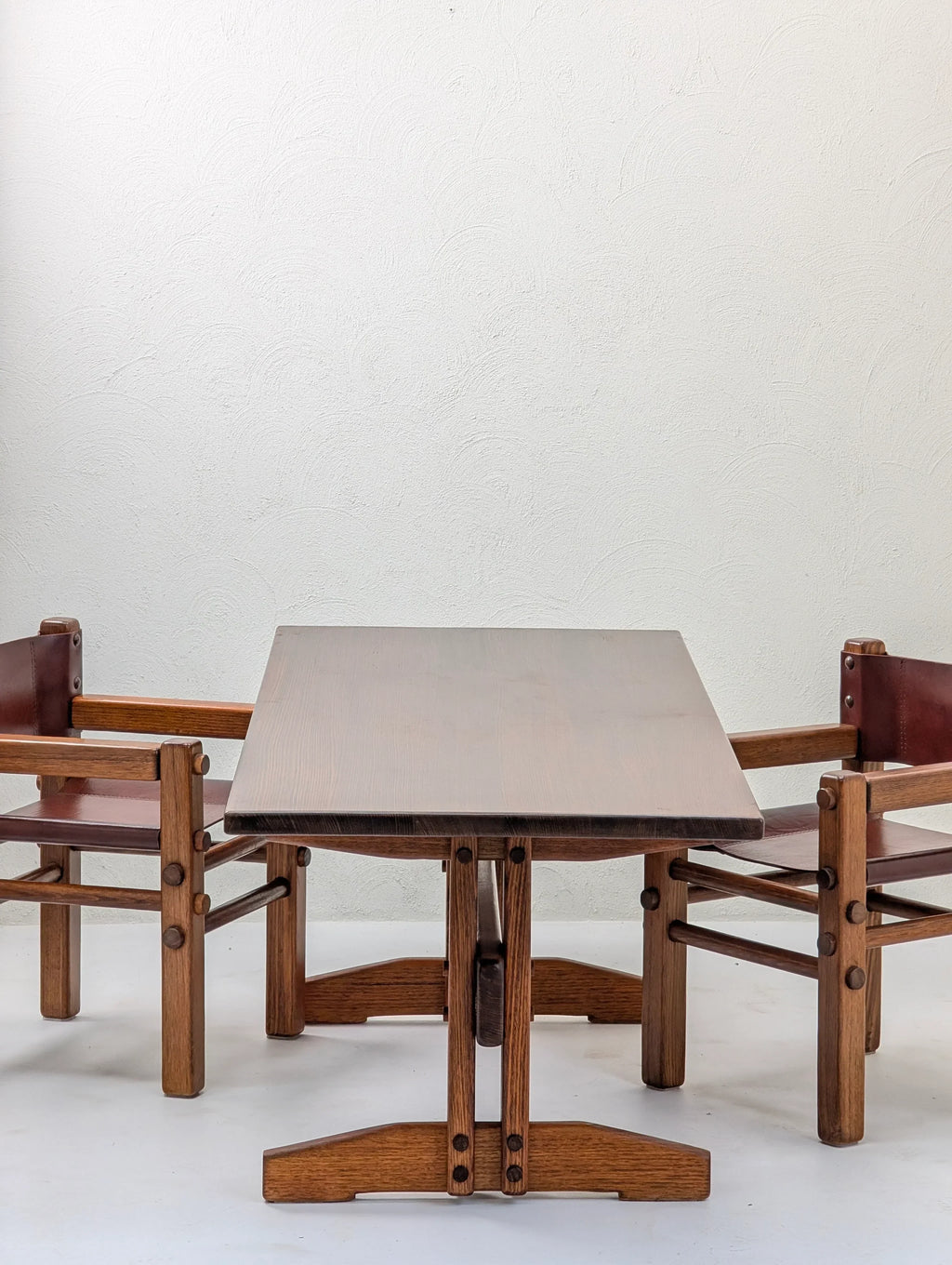 Vintage wooden dining table set with two brown leather chairs against a white textured wall
