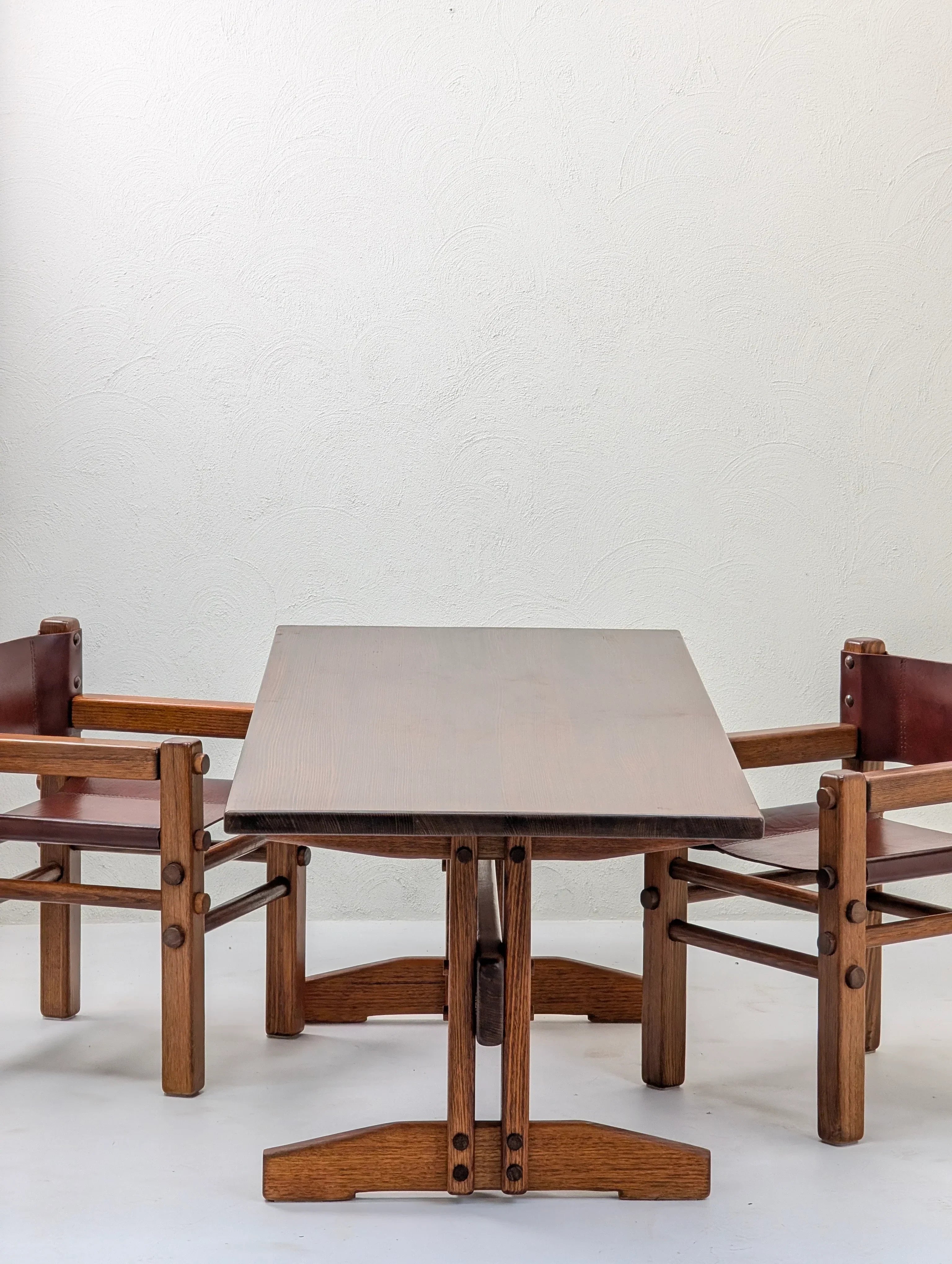 Vintage wooden dining table set with two brown leather chairs against a white textured wall