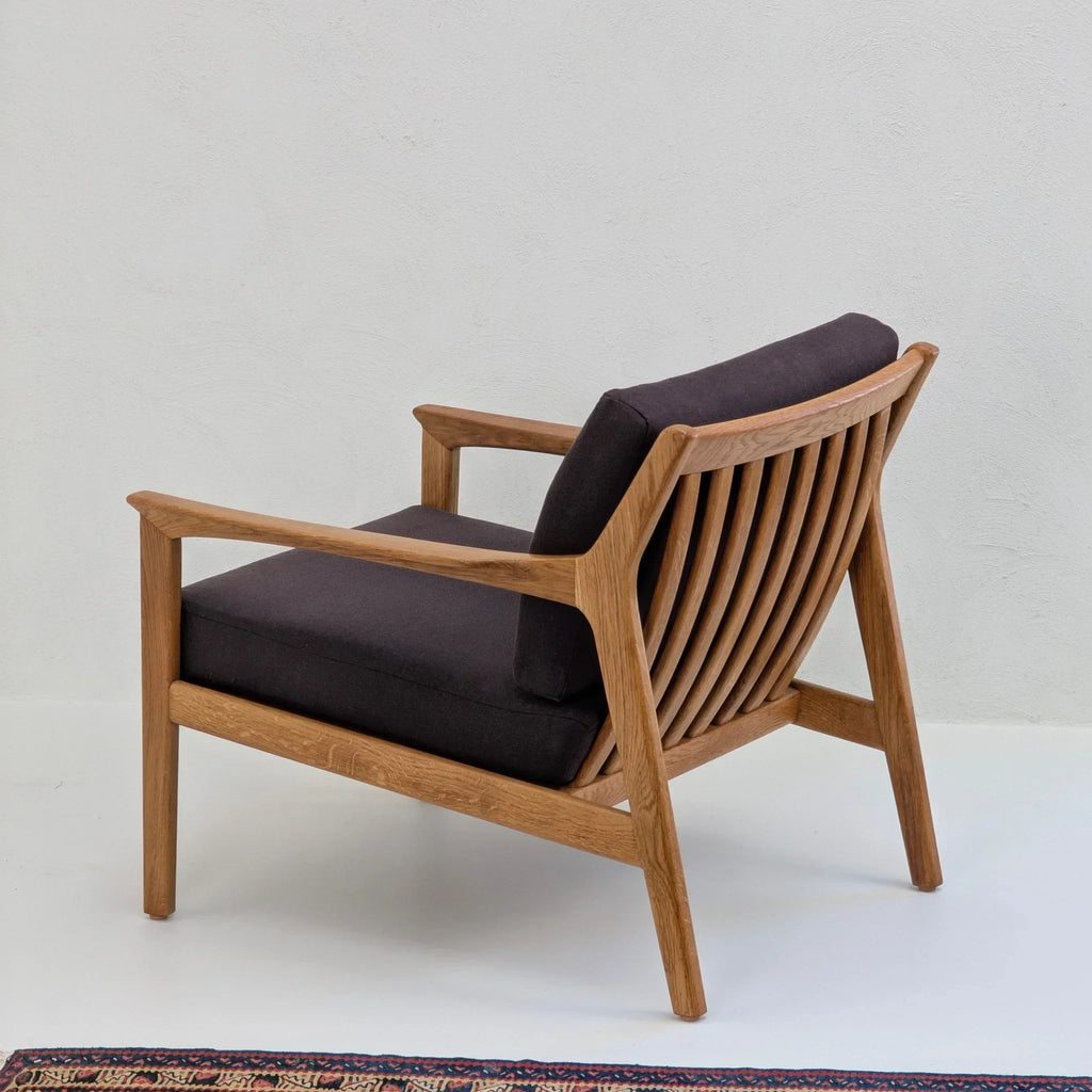 Modern wooden lounge chair with black cushions on a light floor near a patterned rug