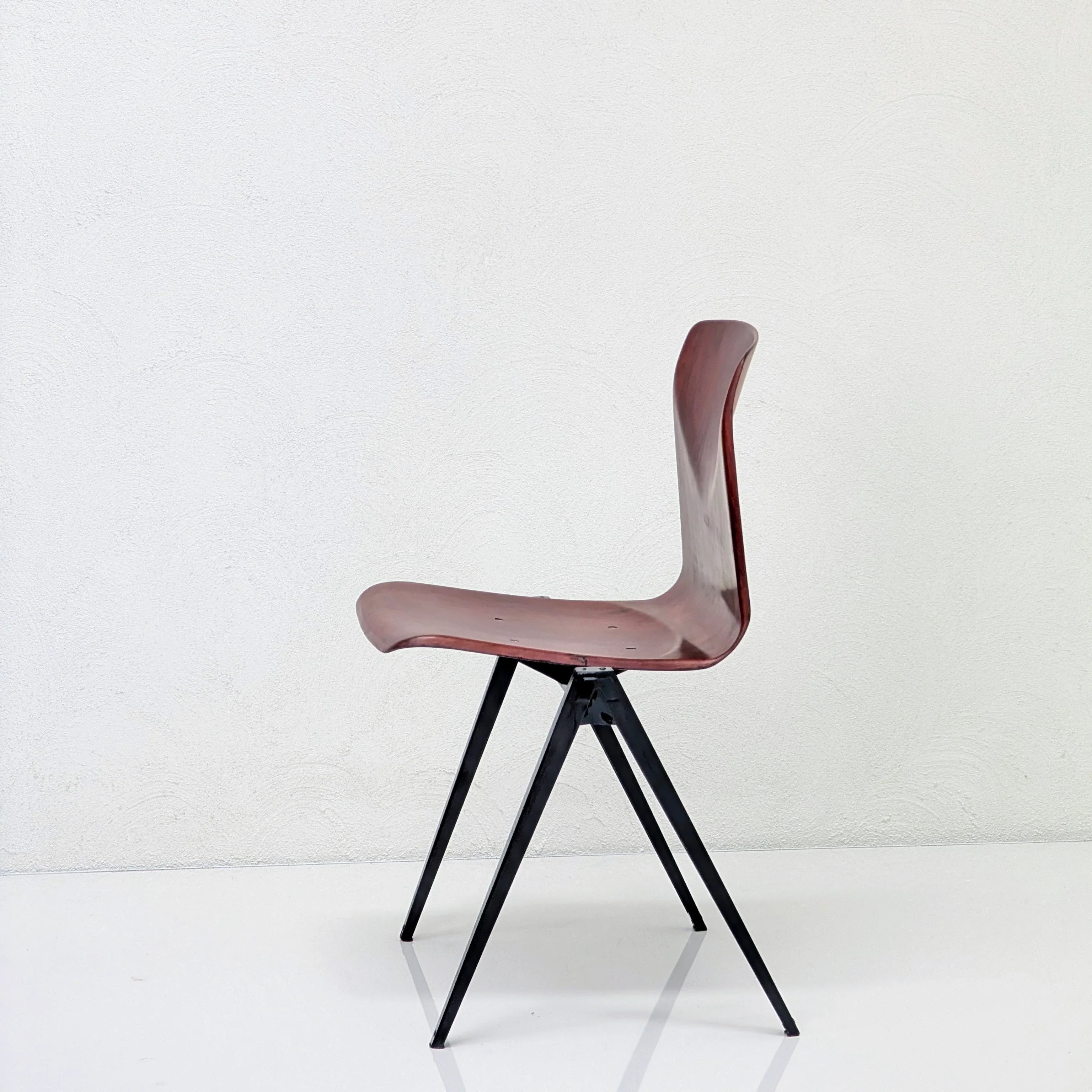 modern minimalist chair with curved wooden seat and black angled metal legs on white background