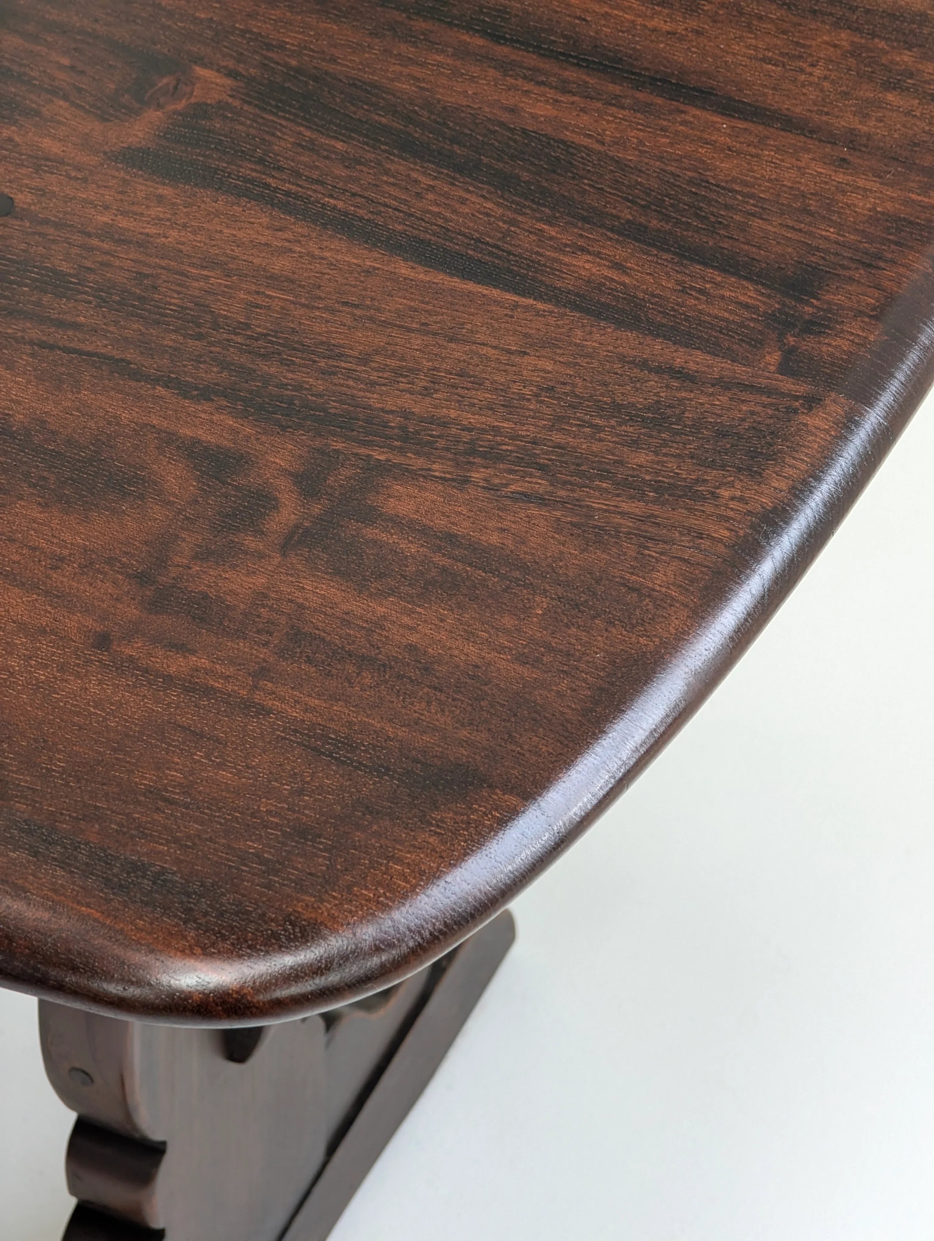 Close-up of polished dark brown wooden table corner with visible wood grain and curved edges