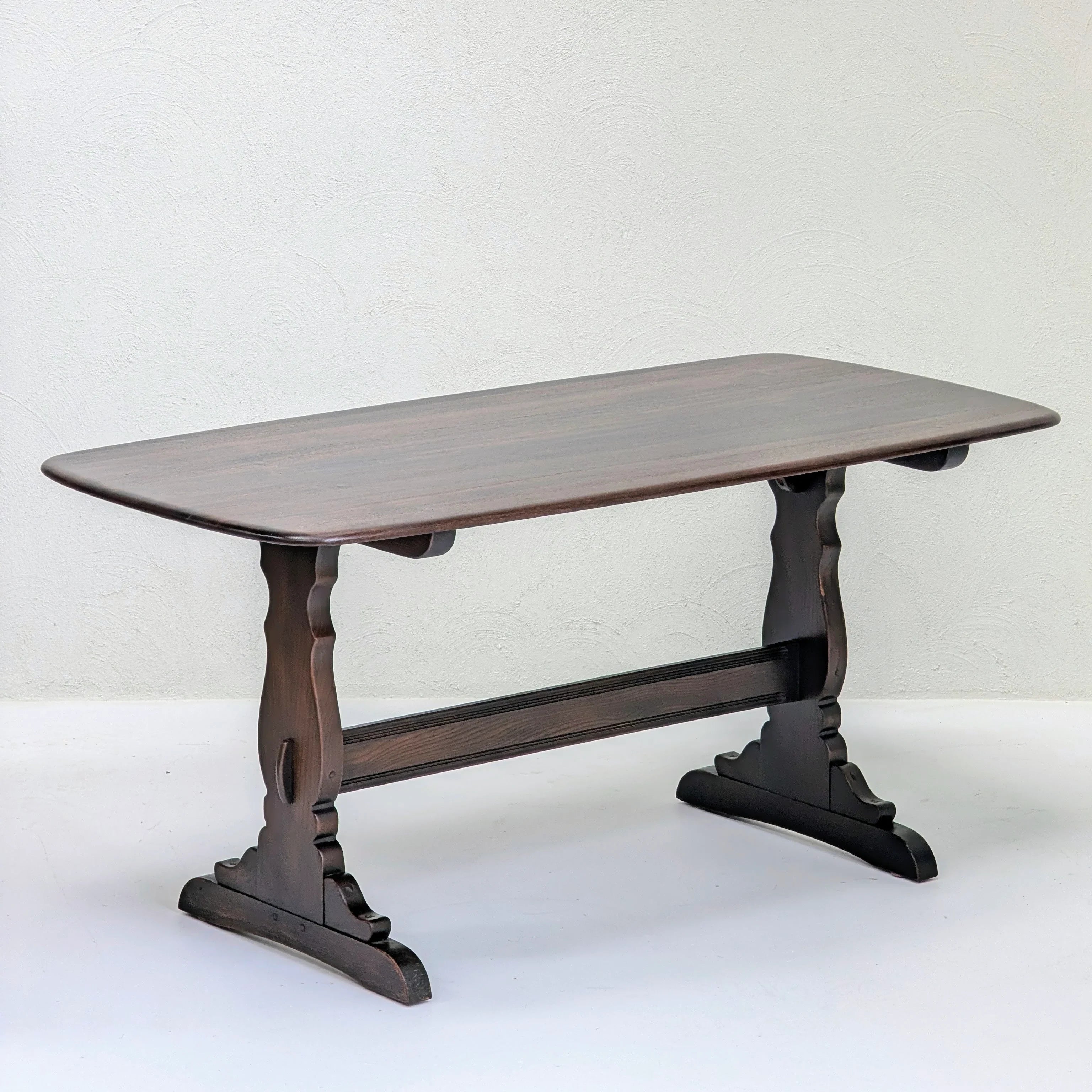 Dark wood rectangular dining table with decorative carved legs against textured off-white wall