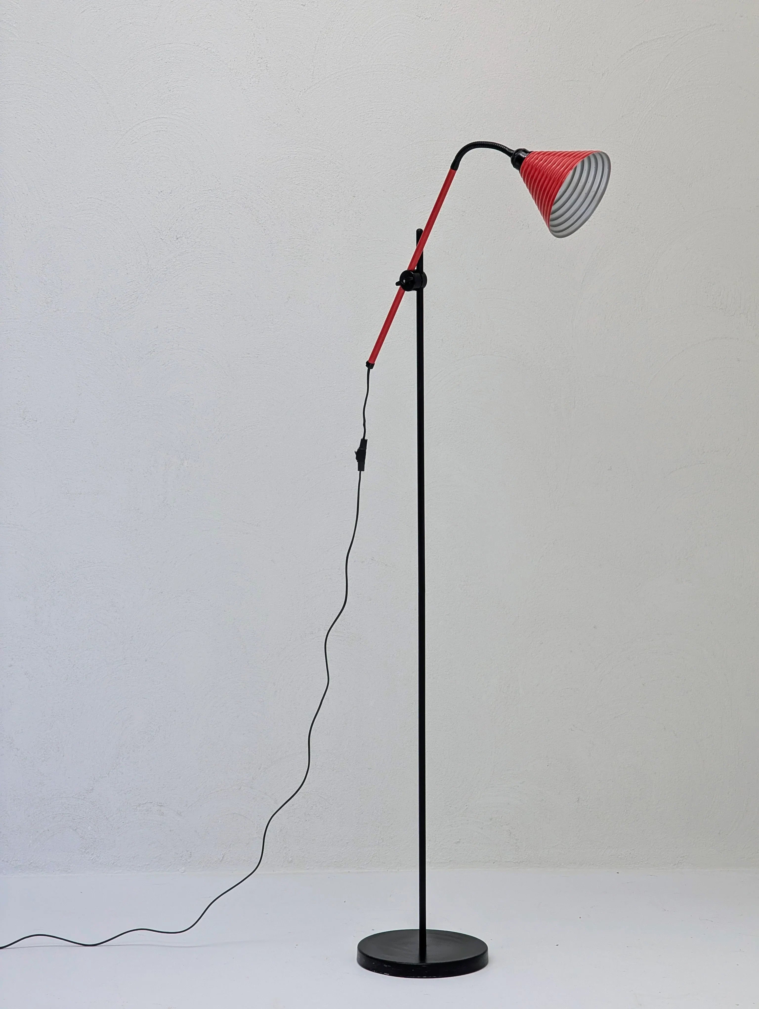 Modern floor lamp with red adjustable arm and striped lampshade against white wall