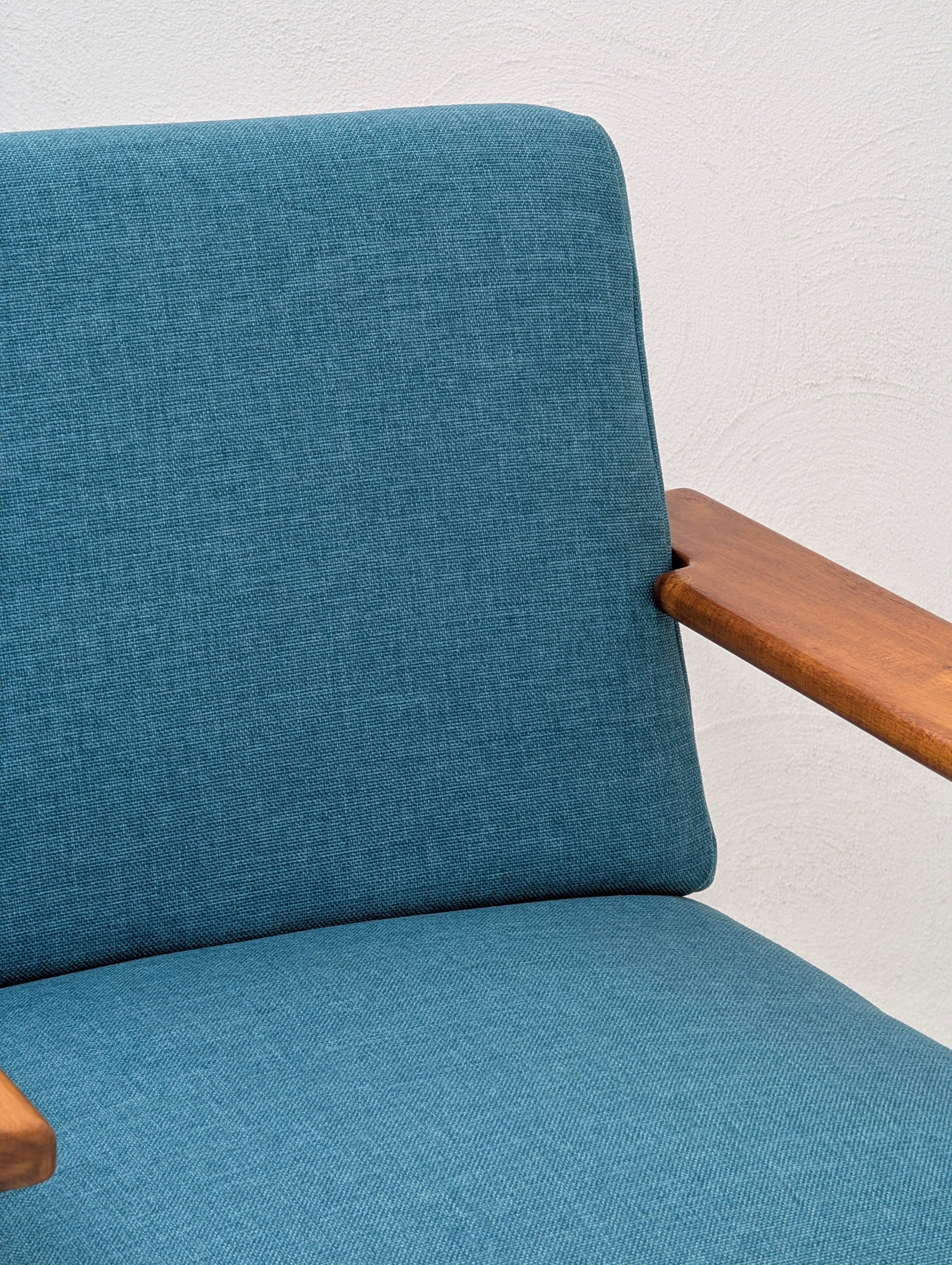 Mid-century modern chair with teal fabric upholstery and wooden armrest against white wall