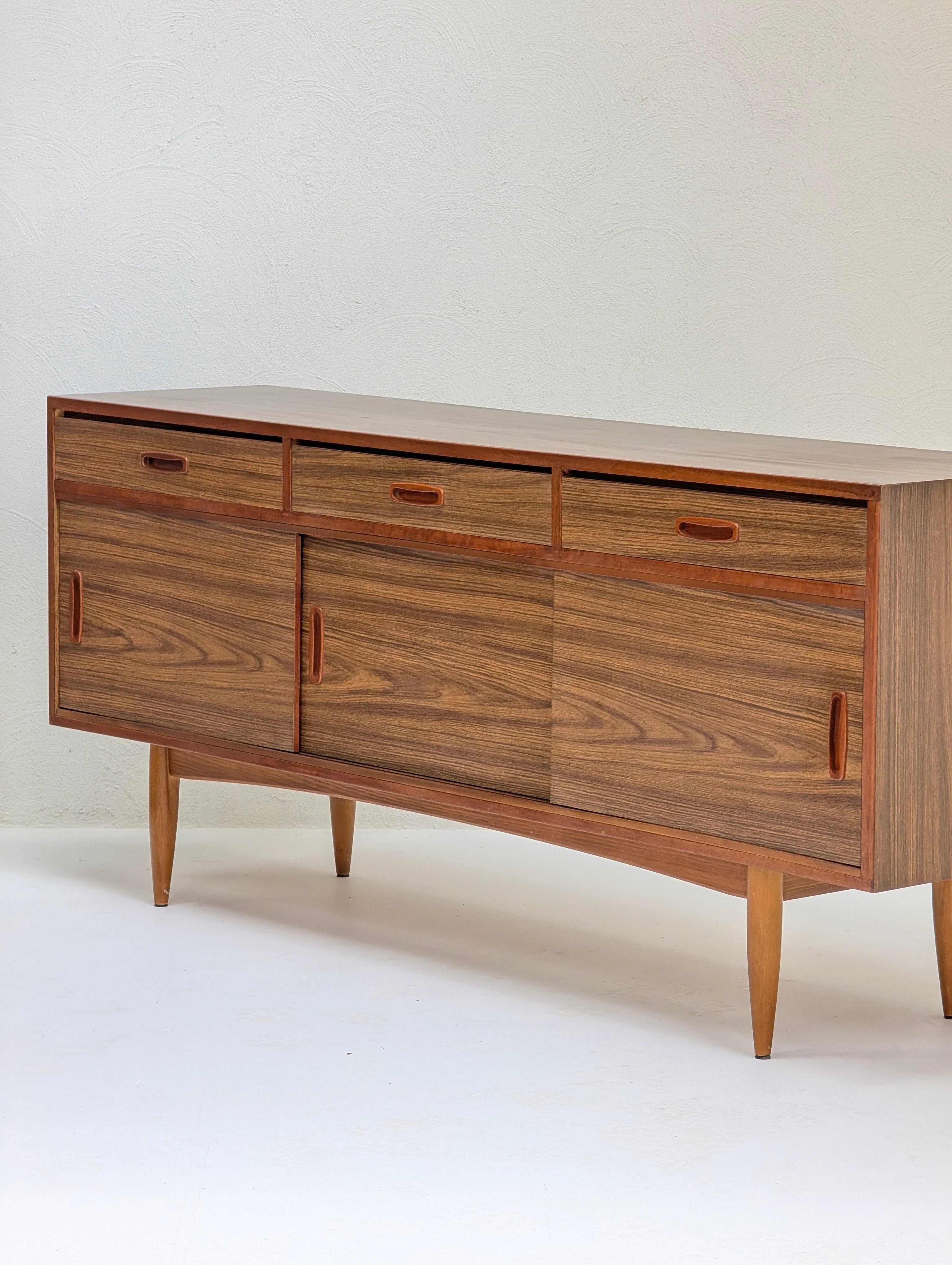 Mid-century modern wooden sideboard with three drawers and sliding doors on tapered legs