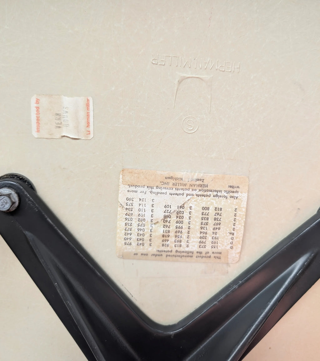 Close-up of beige Herman Miller chair bottom with inspection labels and black metal support frame
